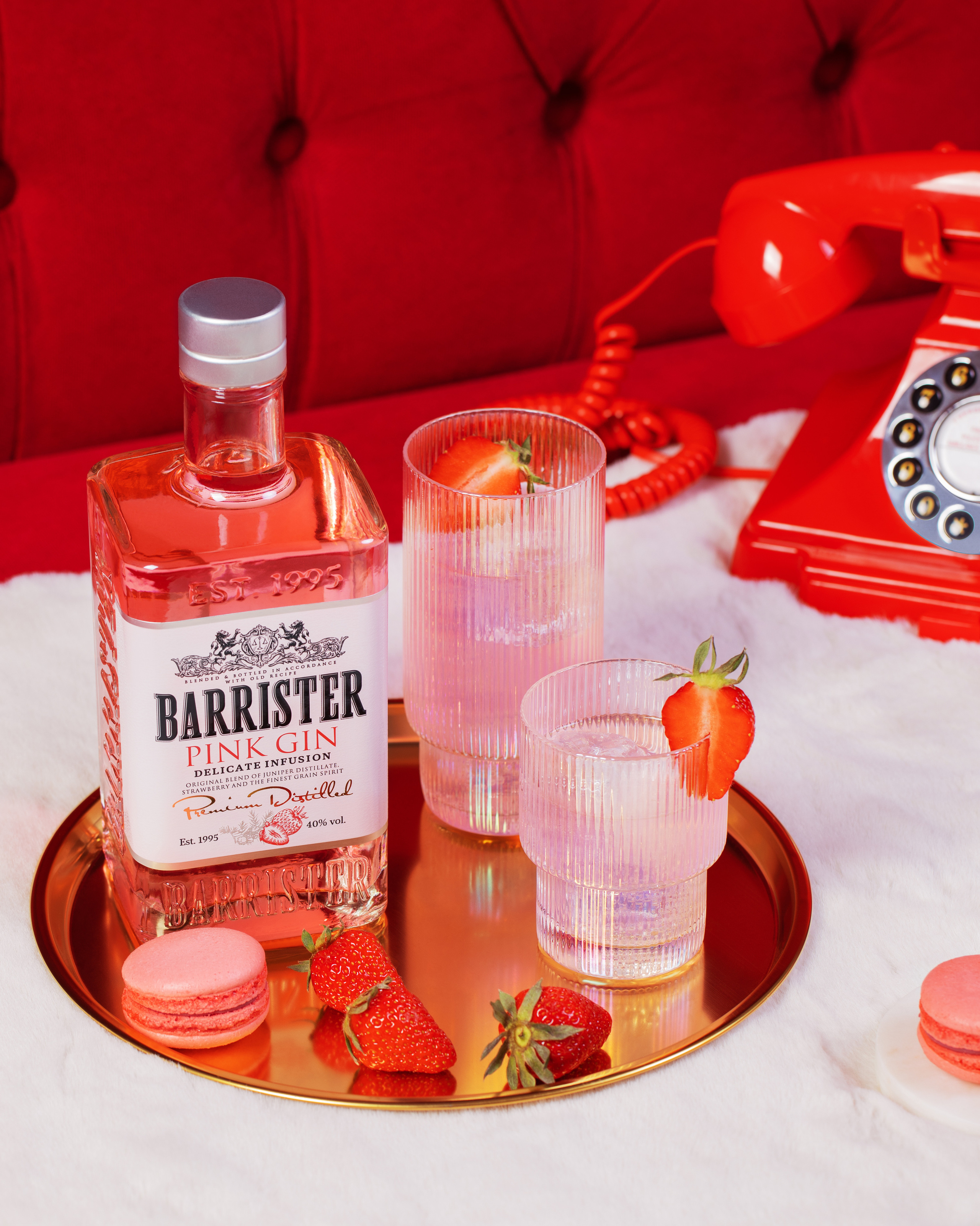 Бутылка с джином стеклянные бокалы с коктейлями на основе джина со свежей клубникой на красном бархатном диване