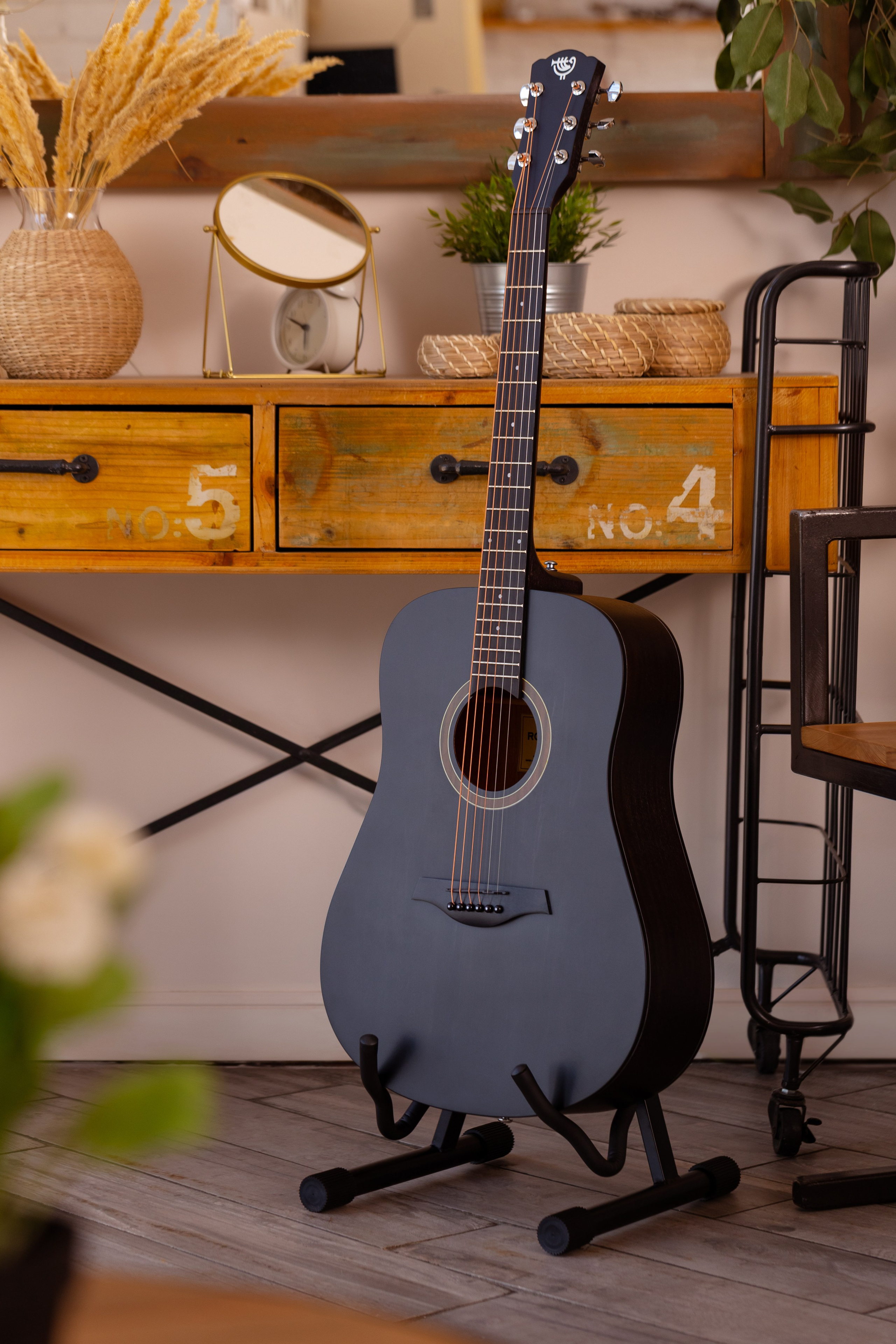 На подставке у стены стоит голубая классическая гитара.