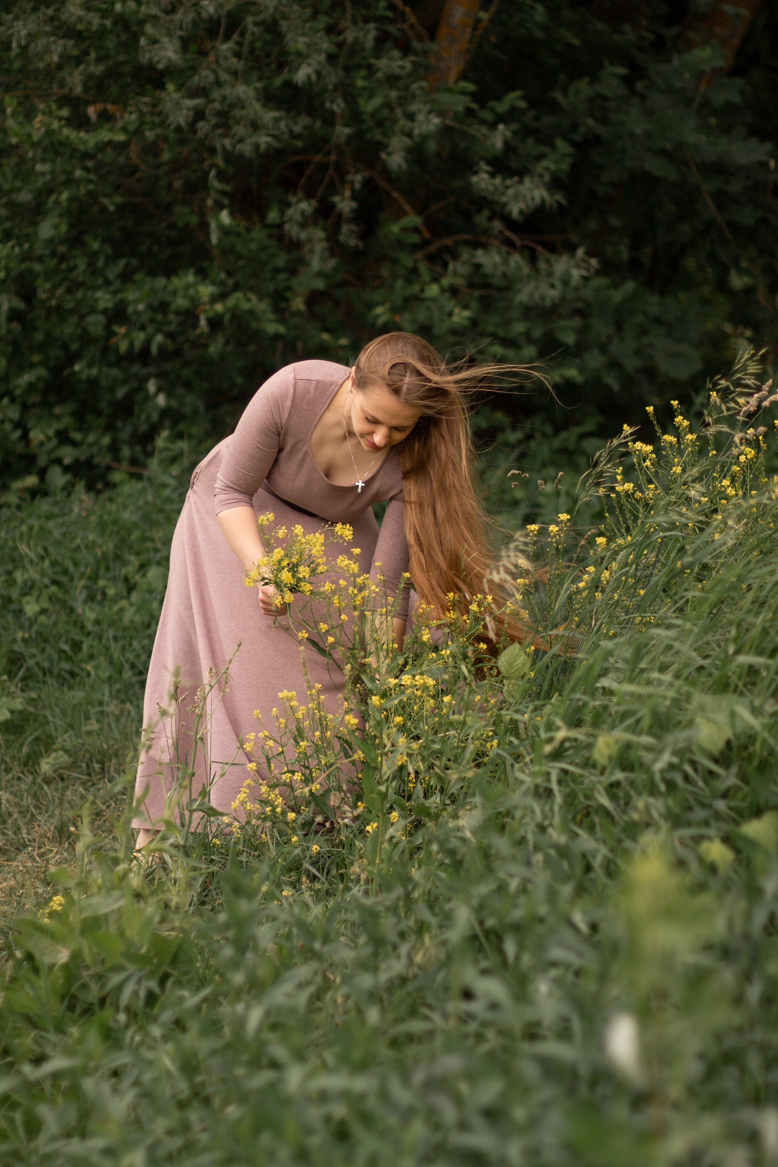 Фотосессия девушки летом, девушка с длинными волосами стоит на берегу реки с букетом желтых цветов, девушка рвет цветы