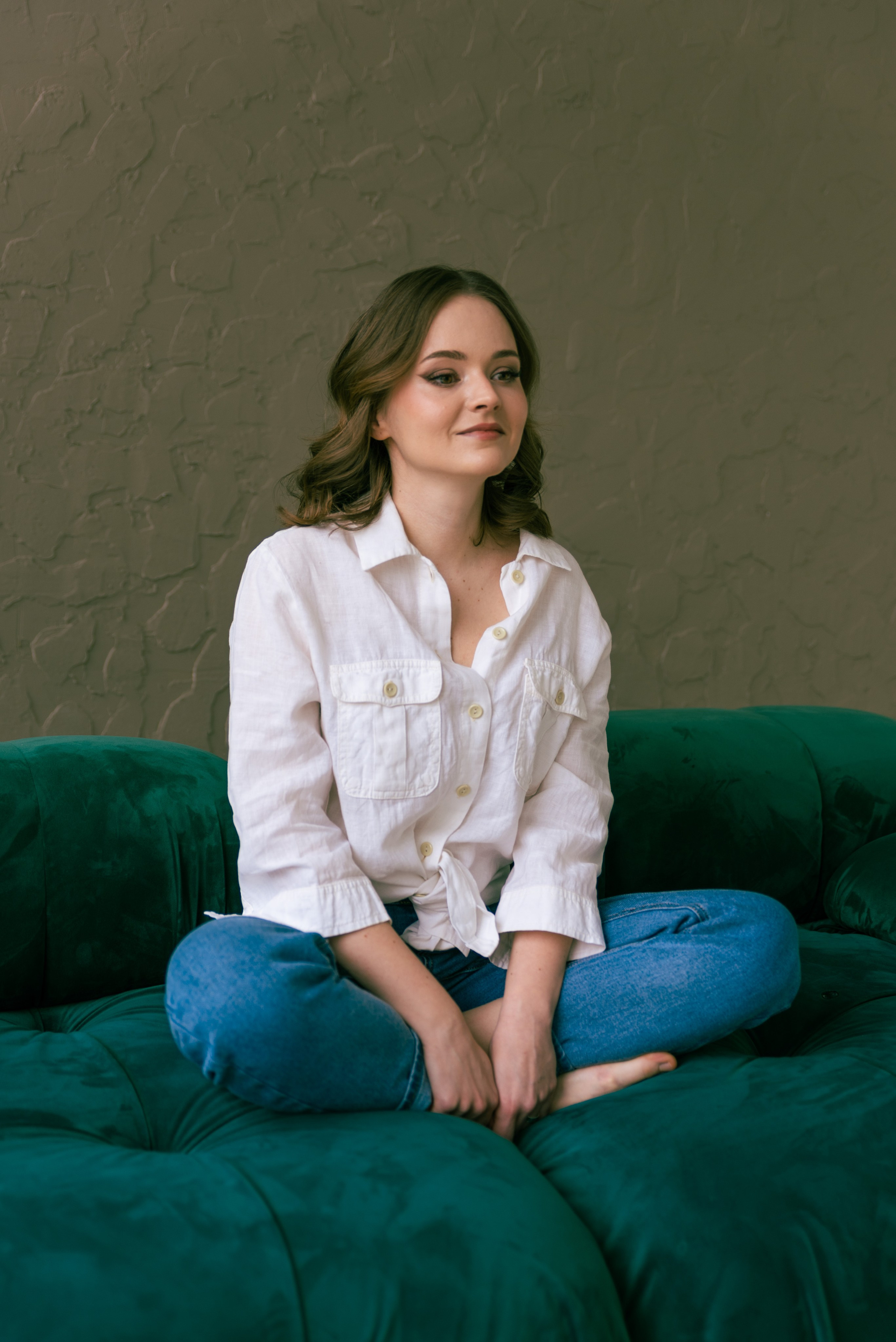 Девушка сидит на диване поджав под себя ноги.