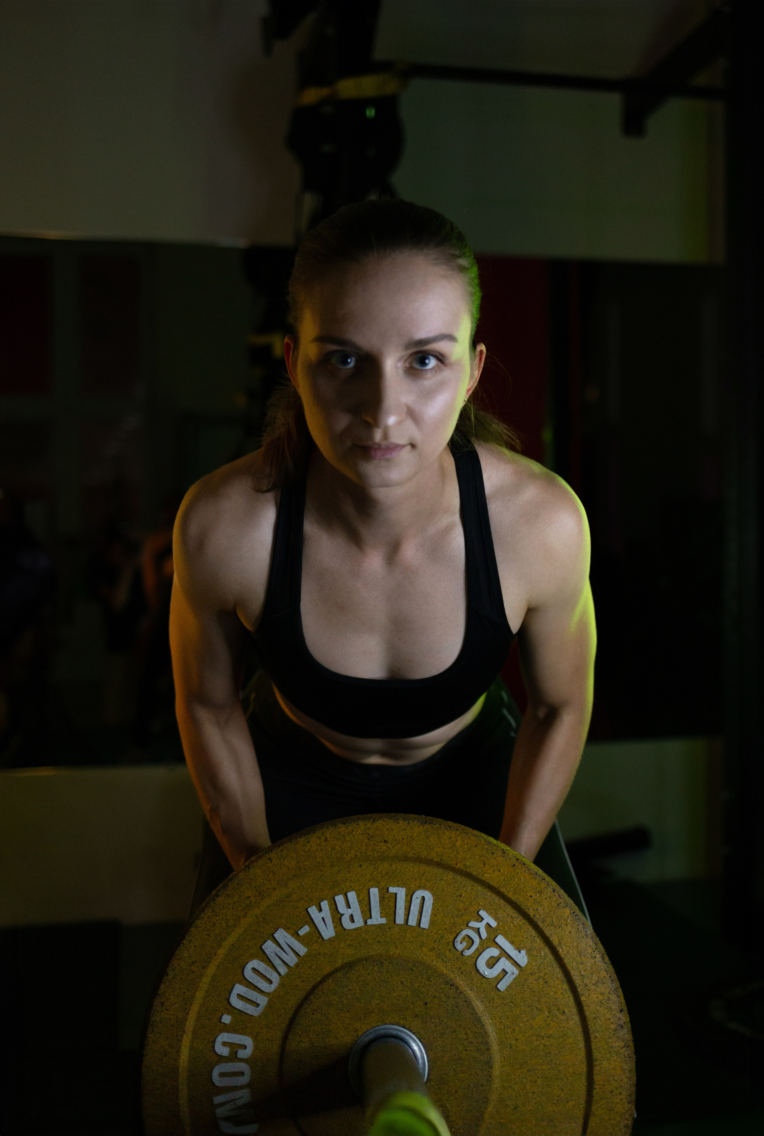 Крупное фото женщины со штангой с желтым блином. Девушка тренер крупно.