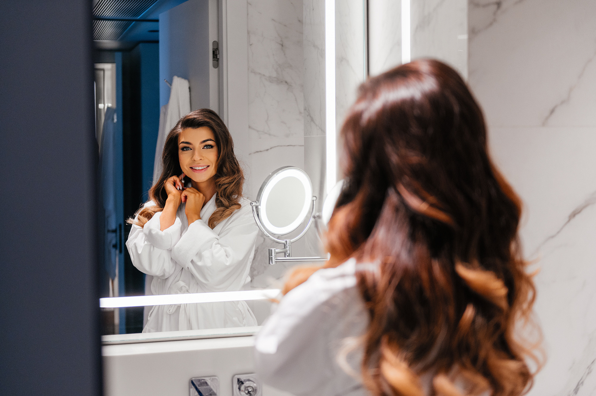 Невеста смотрит на себя в зеркало и надевает серьги.