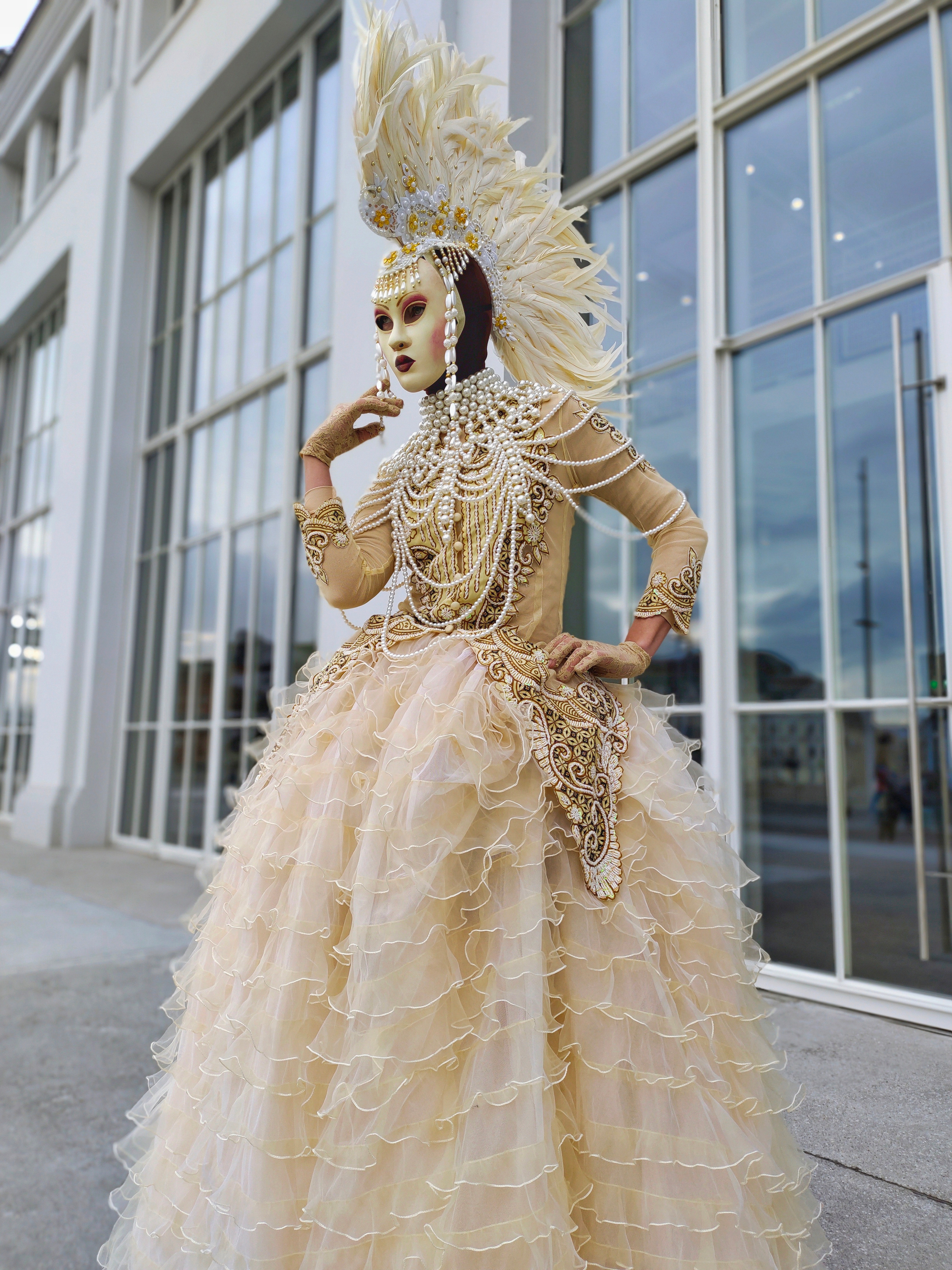 Мим стоит у здания с большими окнами и встречает гостей на мероприятие.