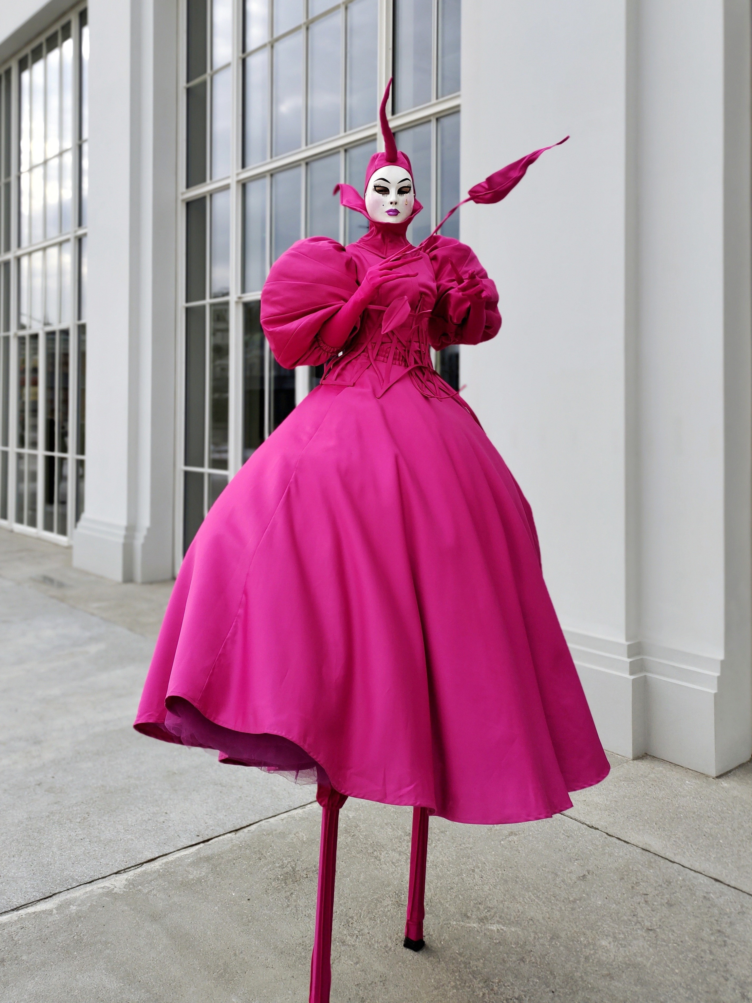 Костюм Ходулиста цвета фуксия создаёт контраст с белым зданием.