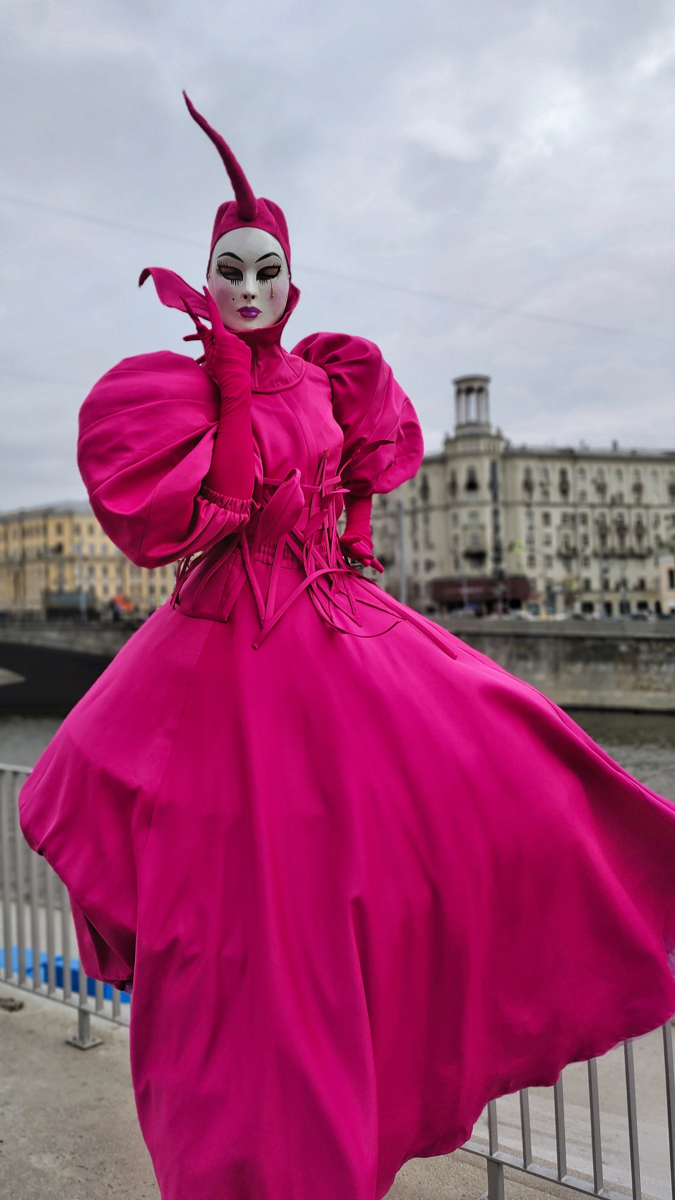 Ходулист в платье цвета фуксия позирует фотографу на встрече гостей.