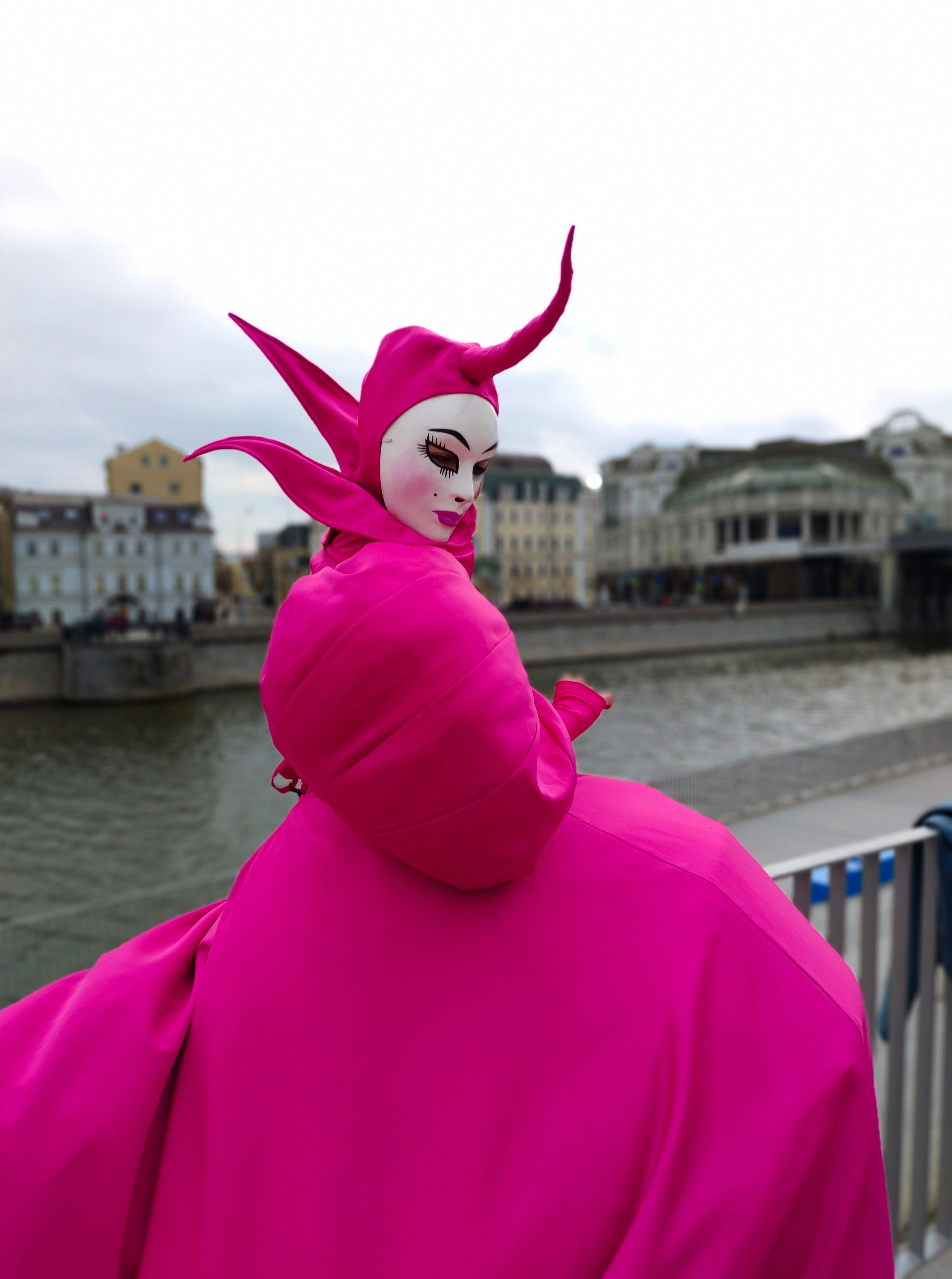 Мим с головным убором с рогом и маской на лице на набережной реки.