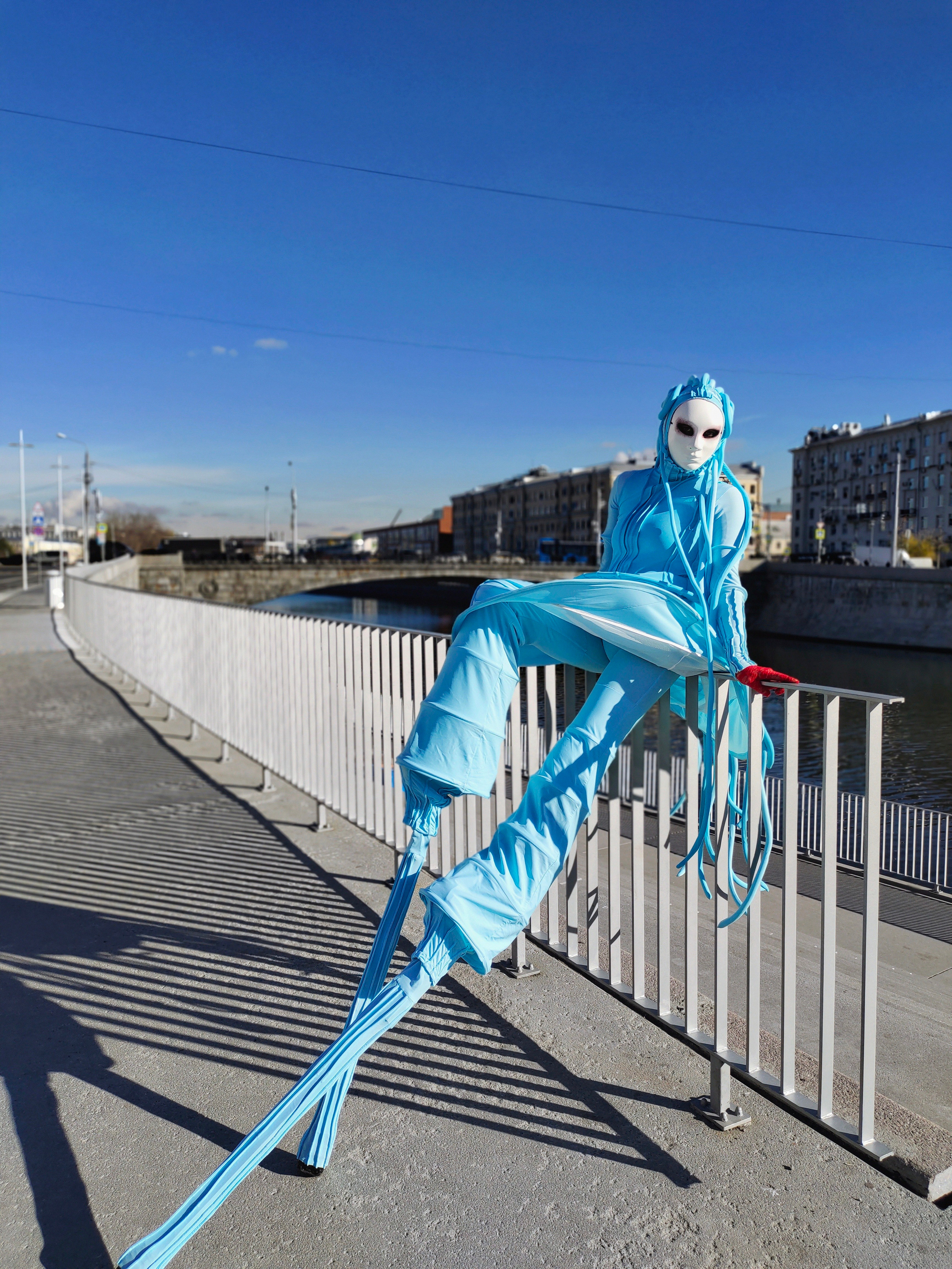 Ходулист в образе инопланетянина сидит на заборе на набережной реки Москва