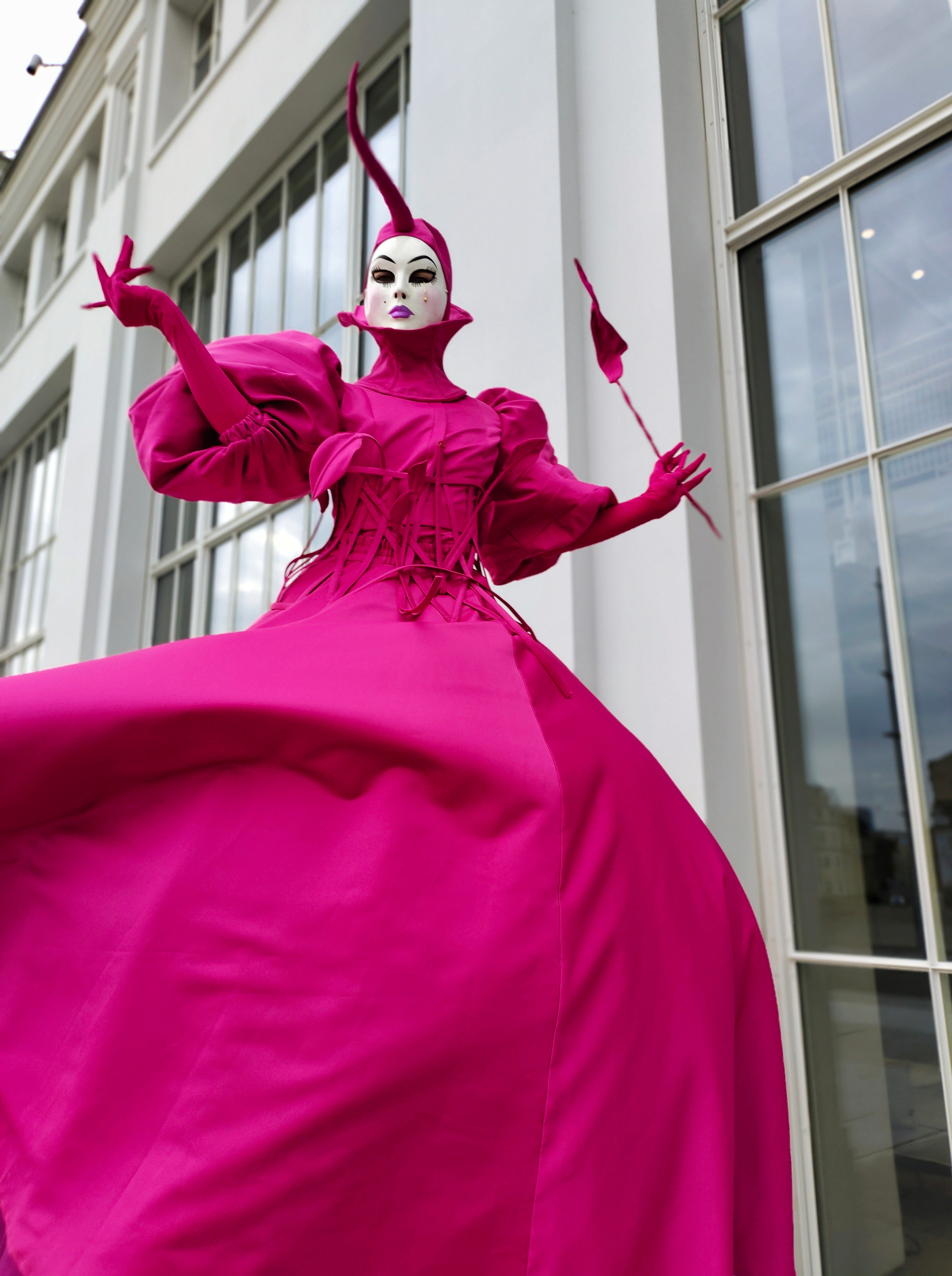 Артист на ходулях встречает гостей в образе фуксия, держа в руке большой лепесток от цветка.