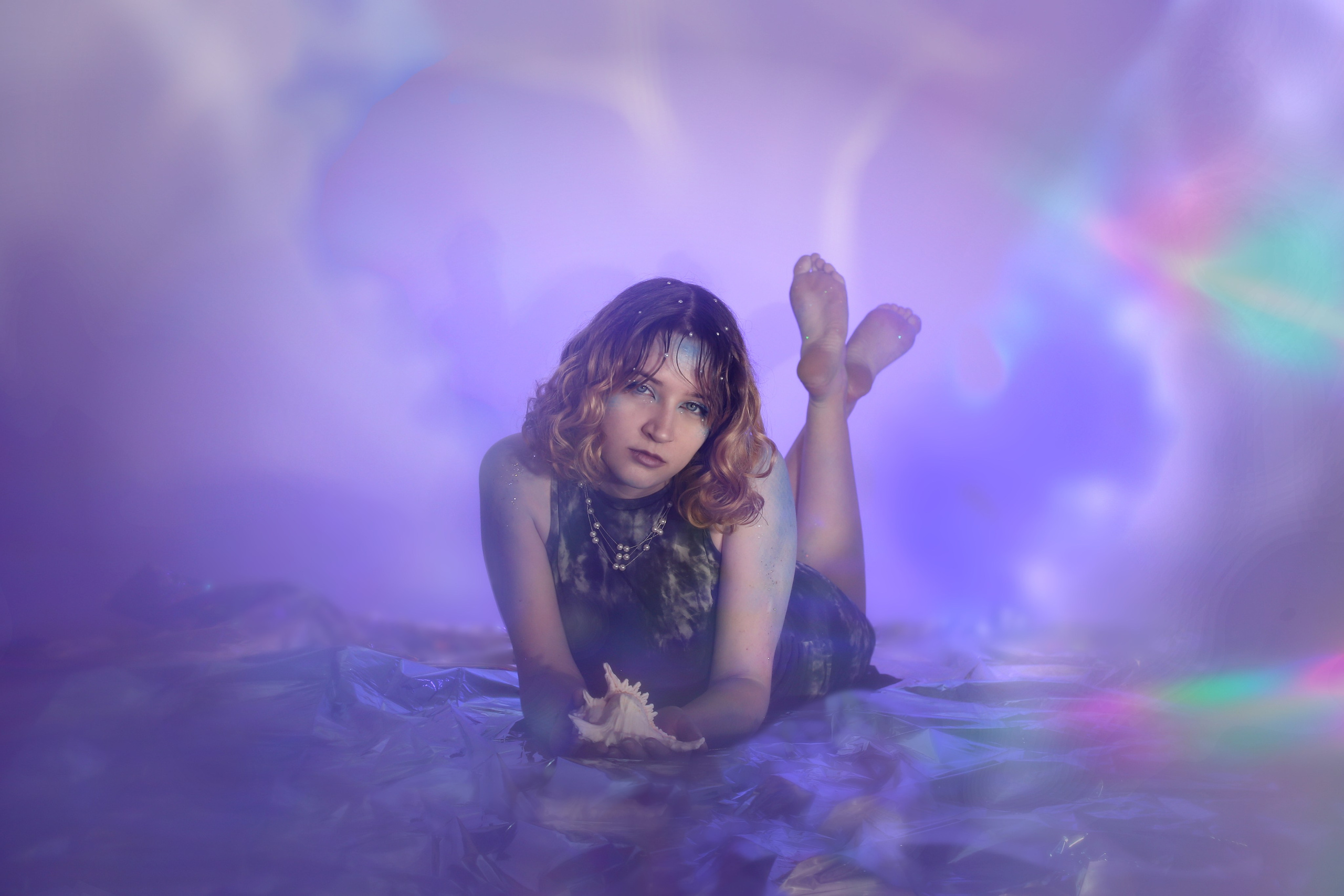 Фотосессия «Ундина»: девушка в черном платье лежит в воде среди радужных бликов