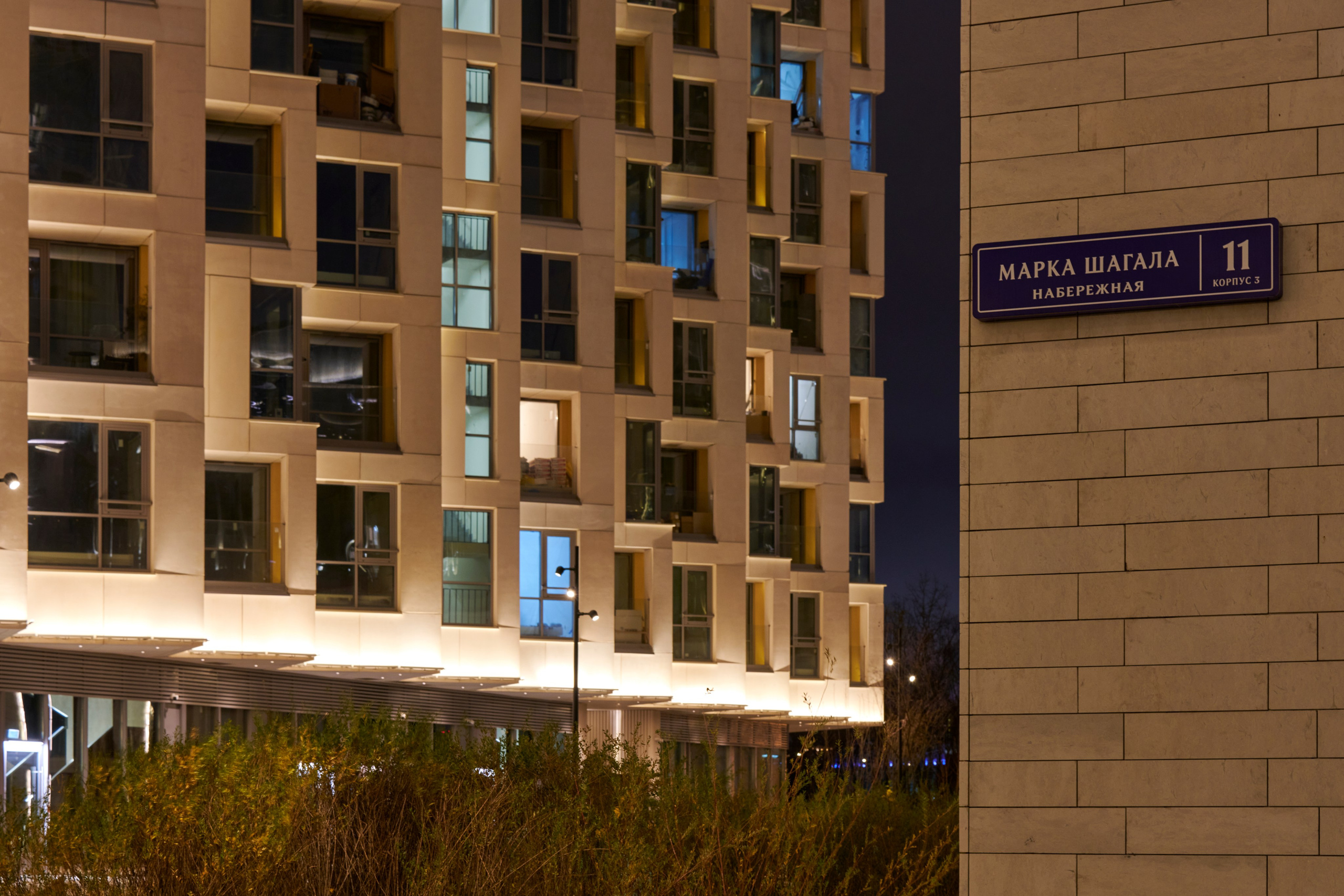 Корпус с подсвеченными этажами, уличная табличка, вечер