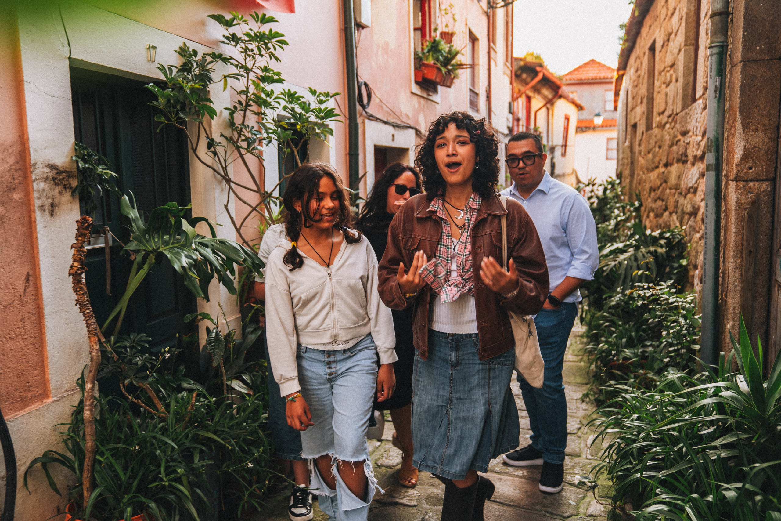 Группа людей гуляет по живописной узкой улочке в Португалии, окружённой старыми домами и зеленью.