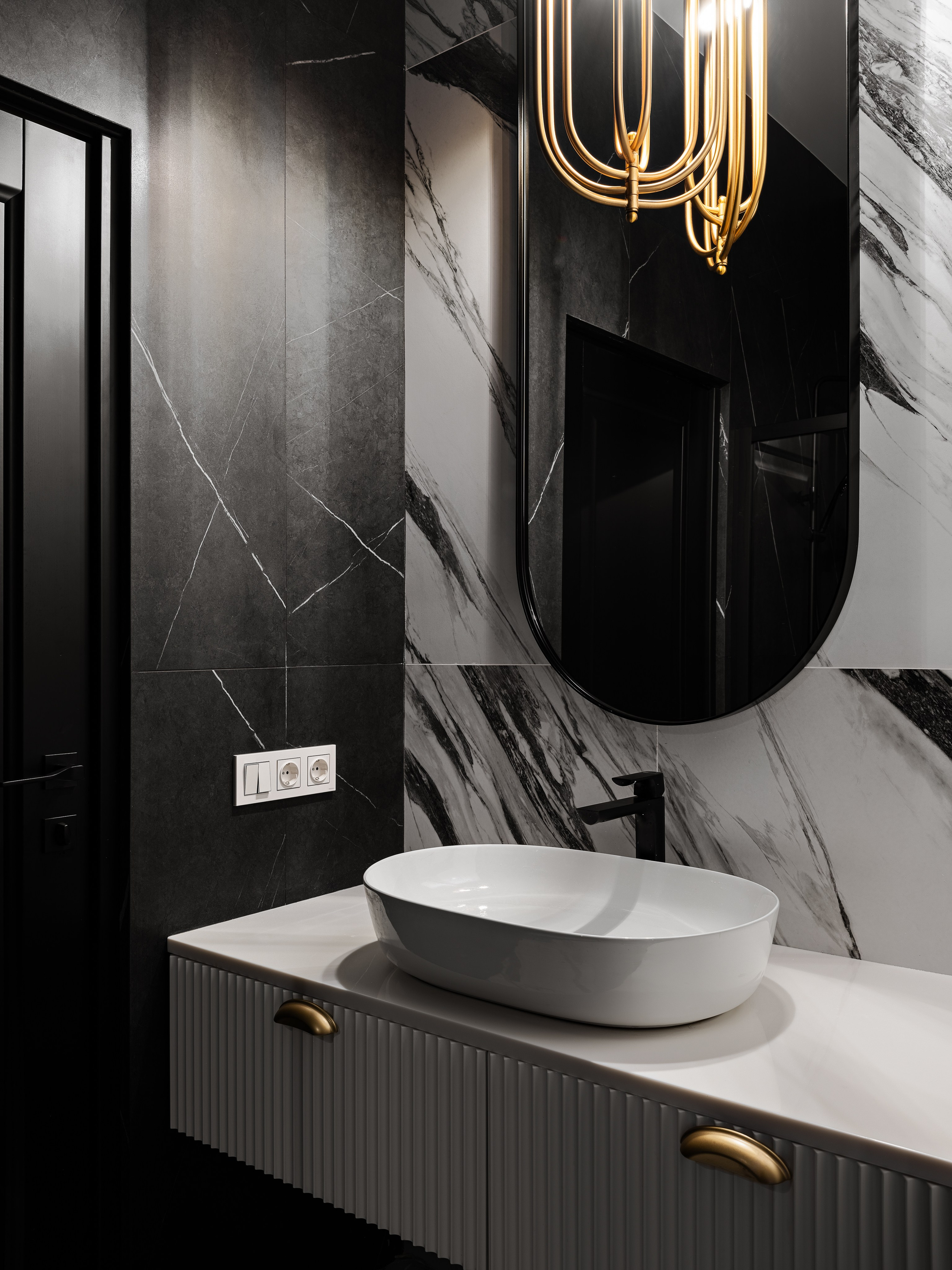 Современный санузел в контрастной гамме: чёрная плитка с белыми прожилками, овальная раковина на рифлёной тумбе с золотой фурнитурой, стильный подвесной светильник, дизайн Василисса Бачева, стилист Наталья Якушева, фотограф Сергей Денисенко.