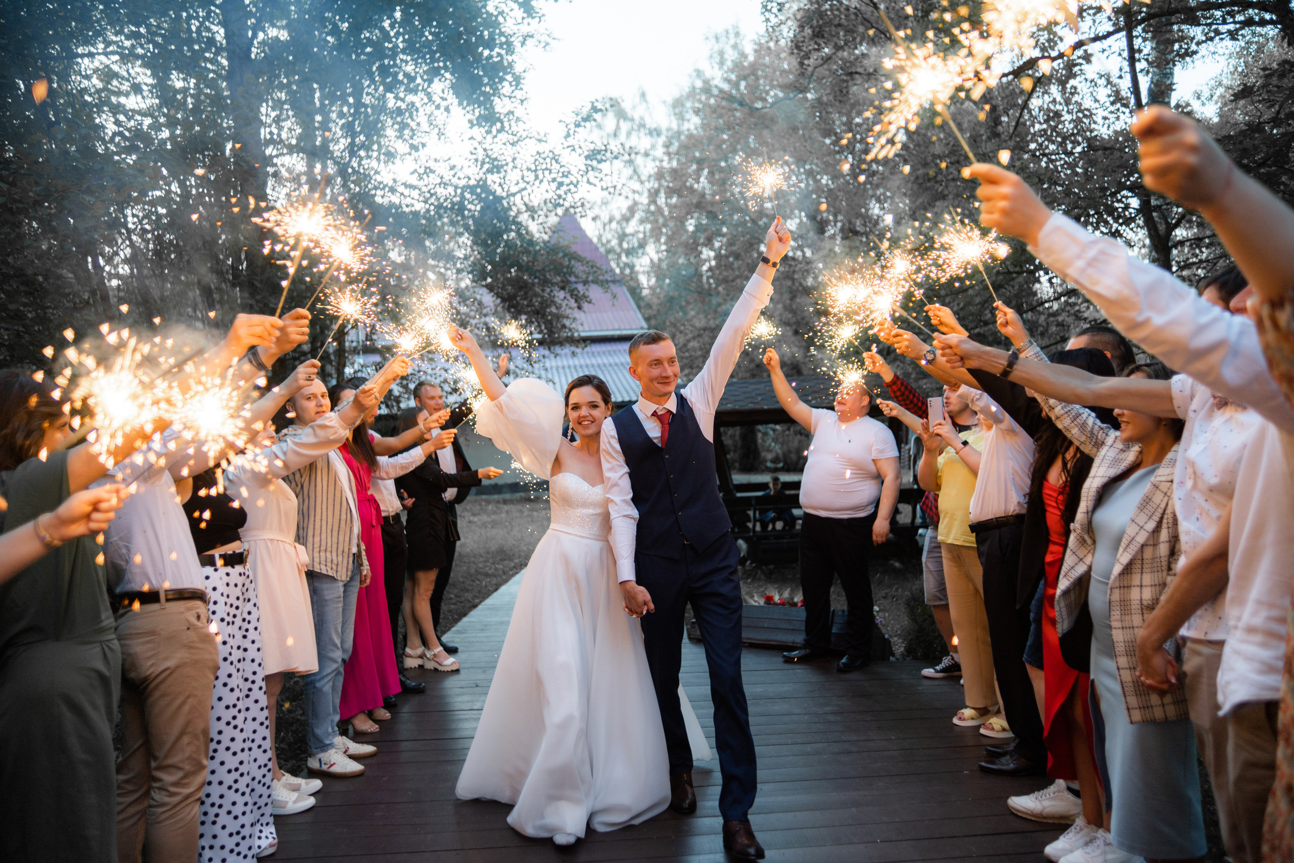 Жених и невеста идут по дороге из гостей которые держут фейерверк