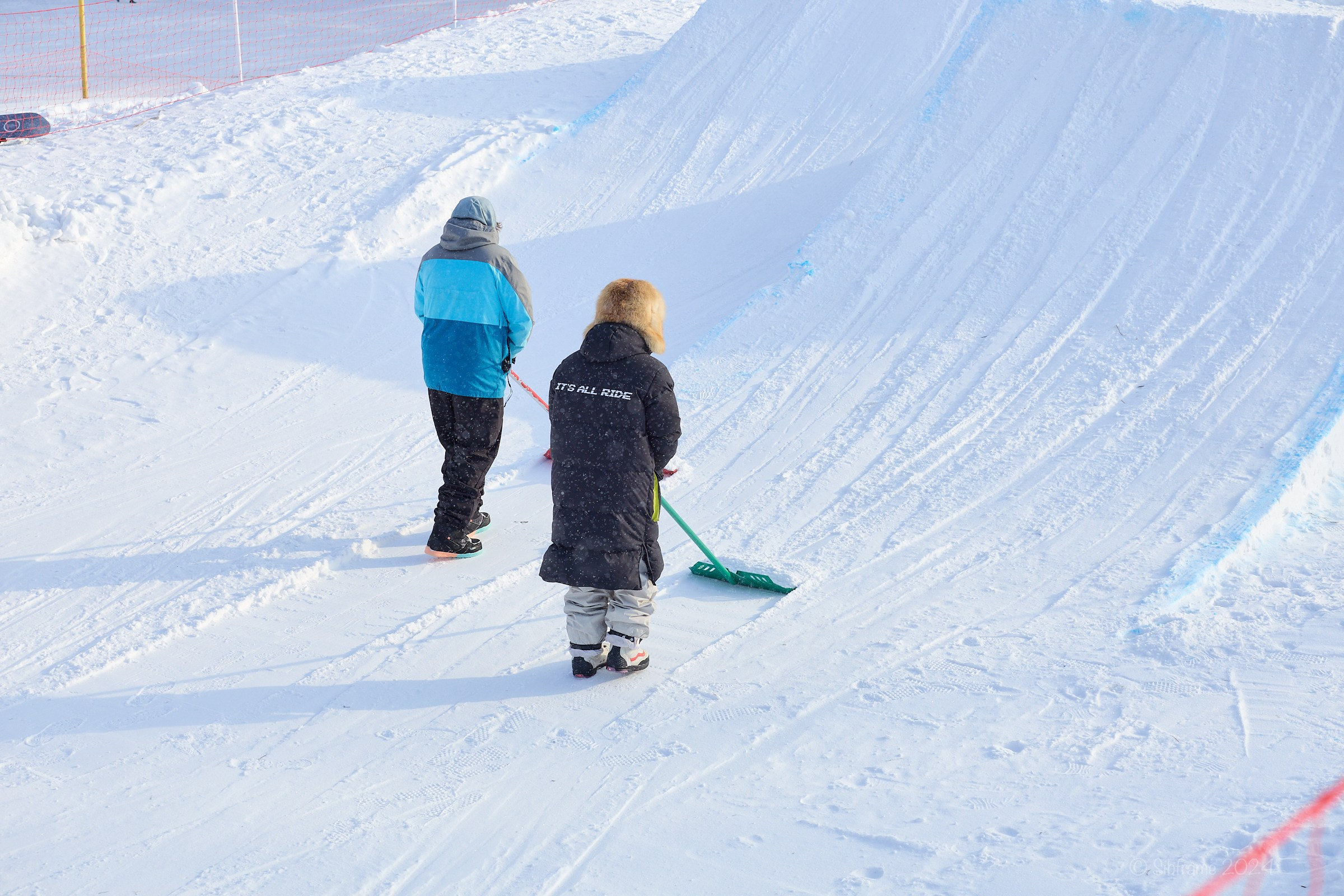 Два человека шейпят вылет биг-эйра для соревнований по сноуборду