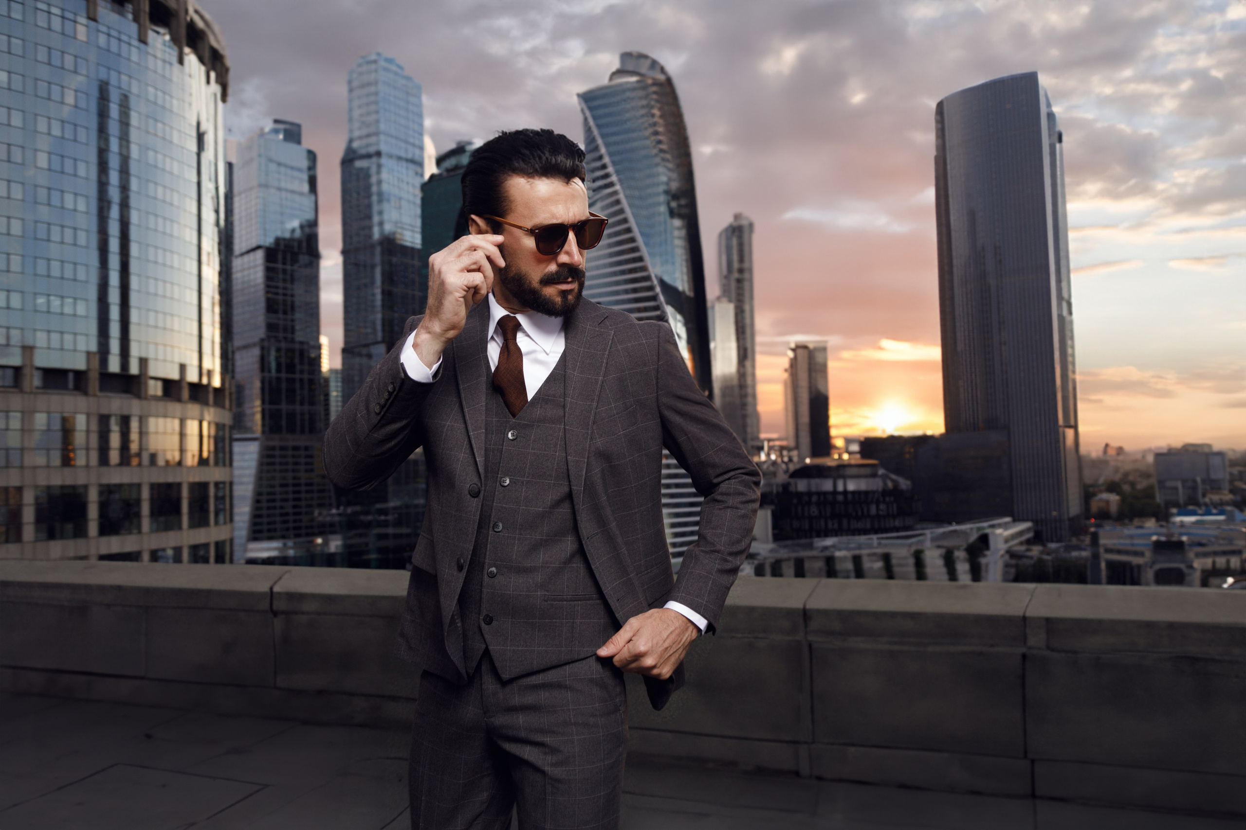 Мужчина в костюме позирует на крыше на фоне заката над Москва-Сити.