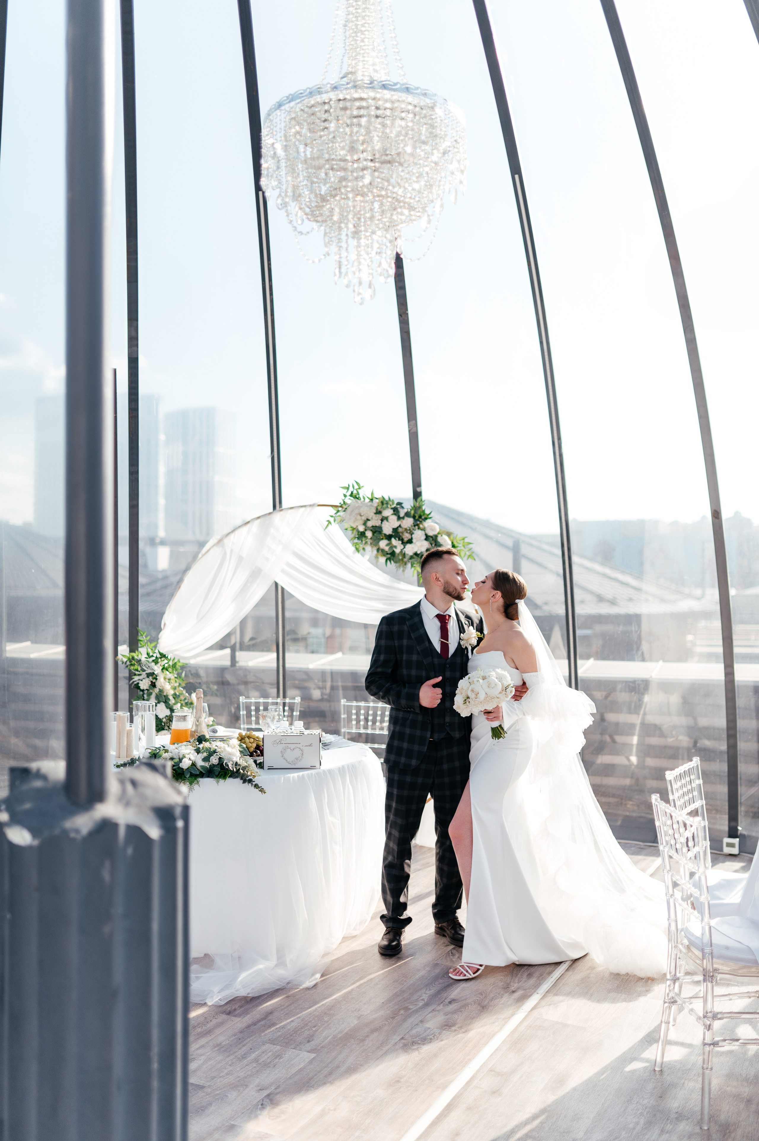 Жених с невестой стоят в очень светлом банкетном зале с естественным светом.