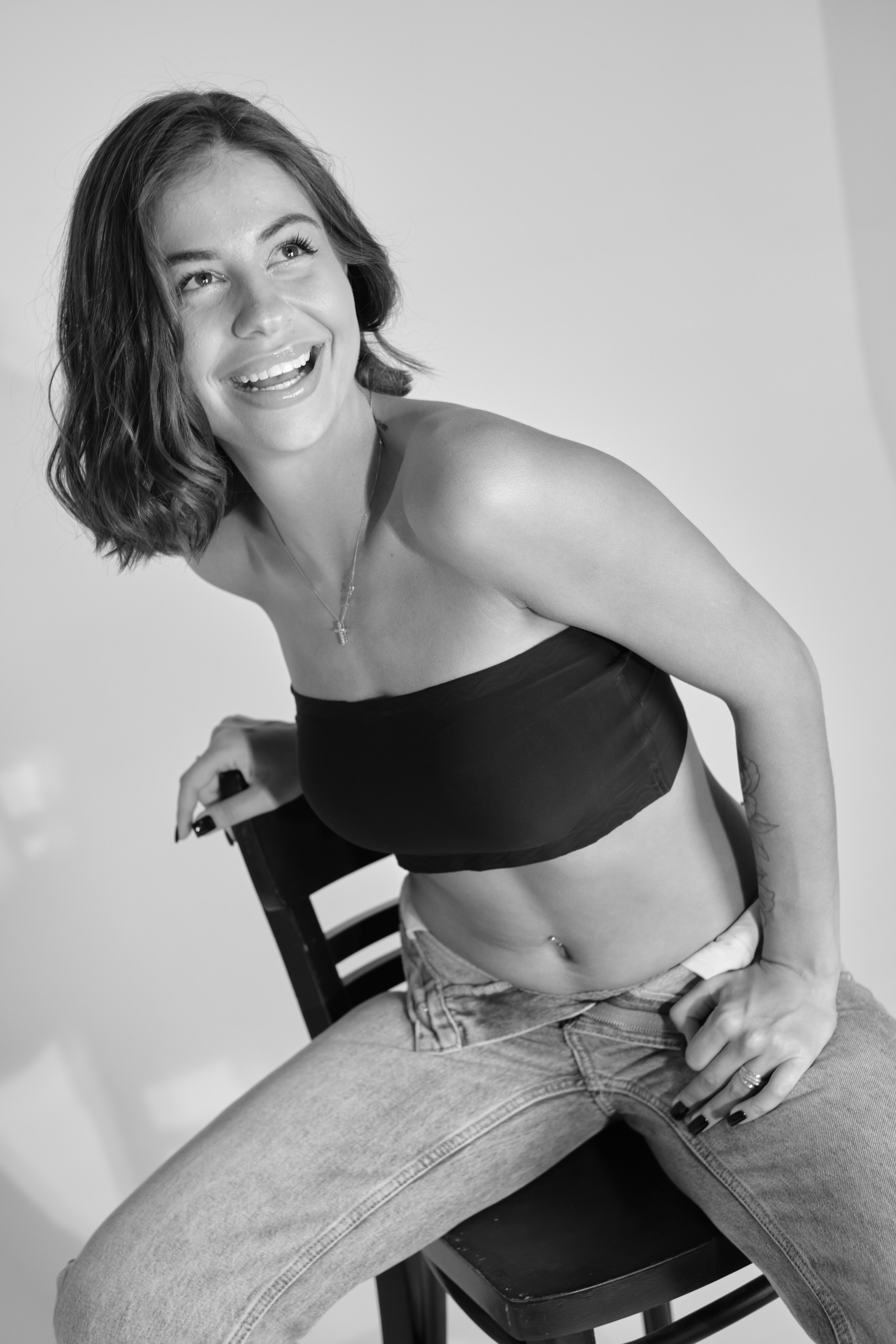 Сьемка в студии для модельного агентства, девушка в джинсах и черном топике сидит на стуле,  ЧБ