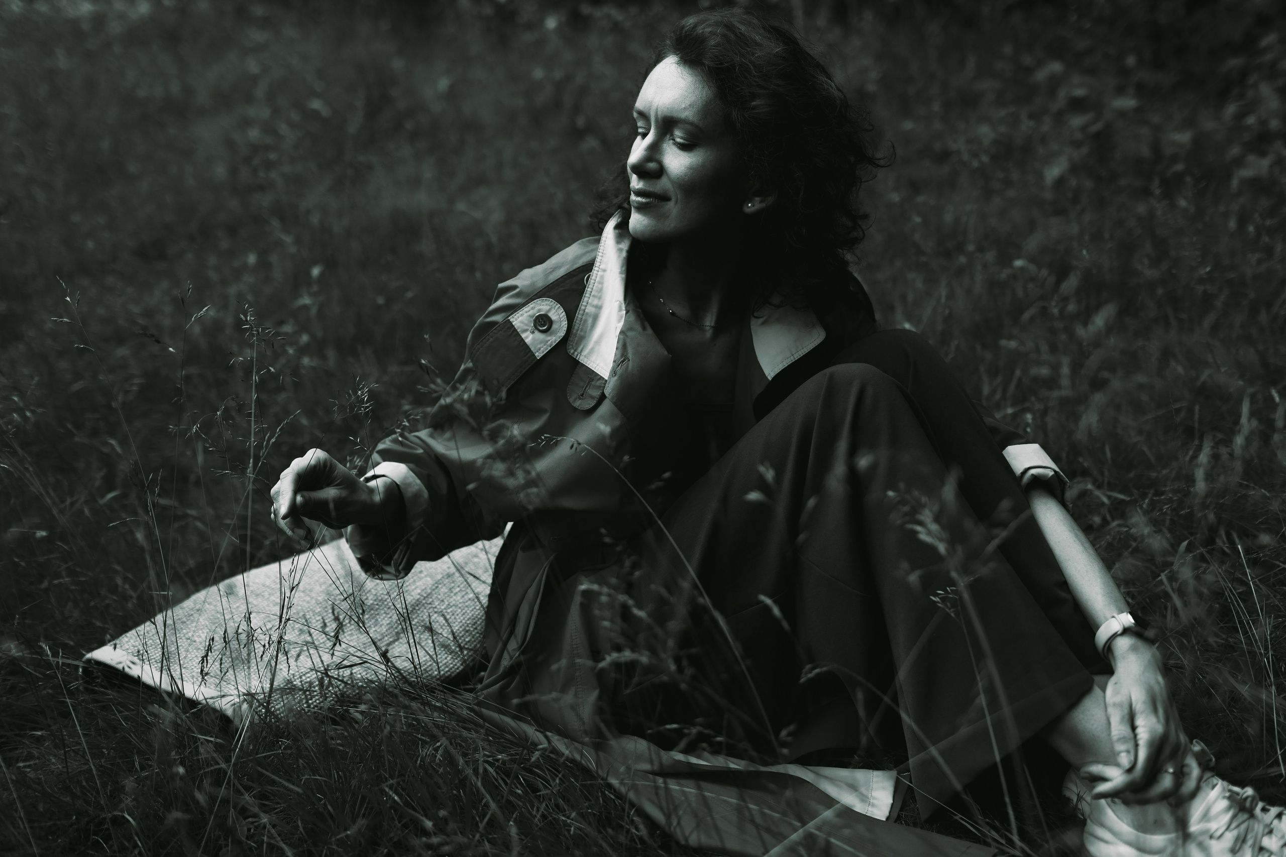 девушка сидит на плетеном ковре в парке и трогает травинки. черно-белая фотография