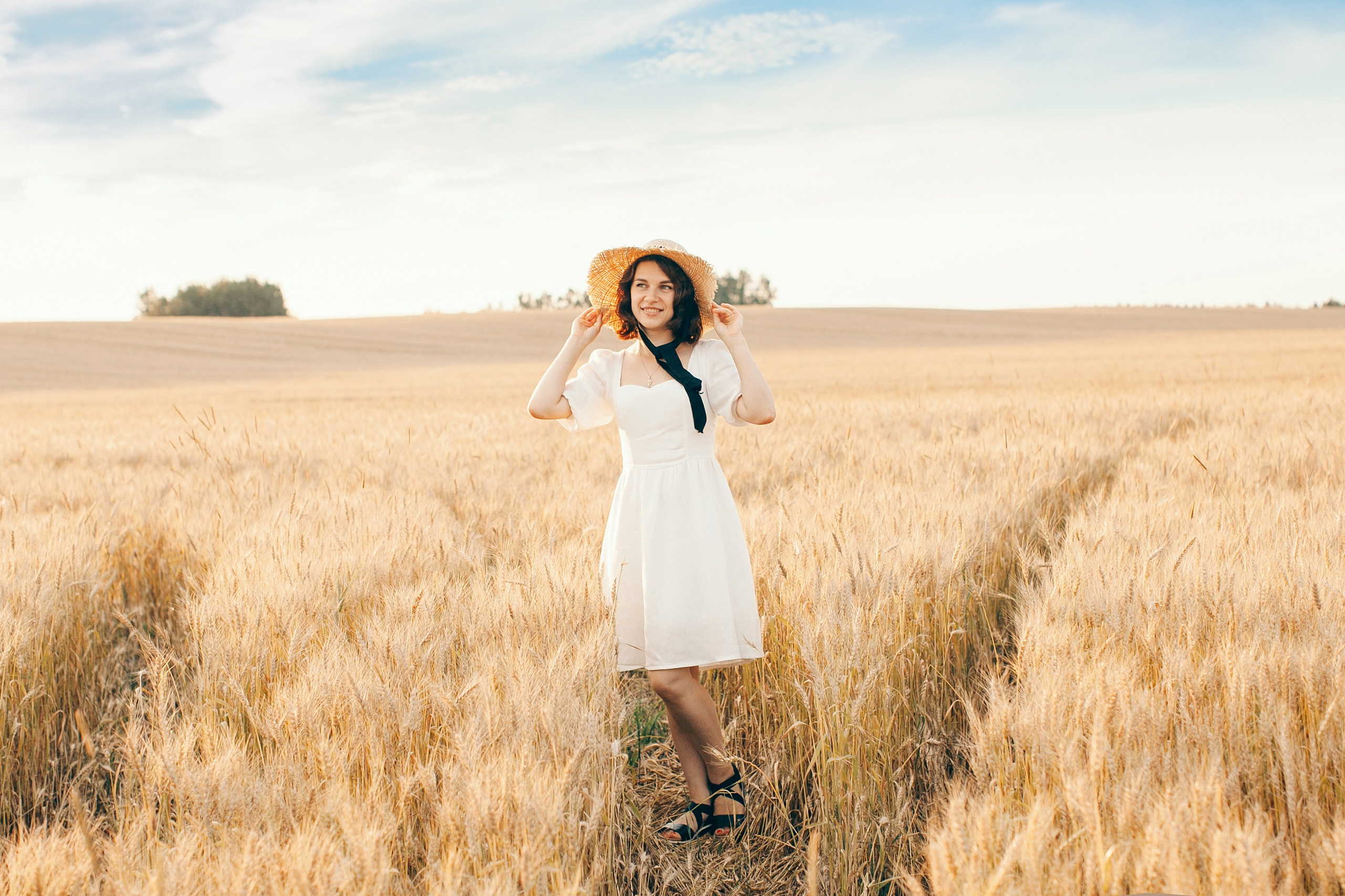 Девушка в шляпке позирует в пшеничном поле на фоне голубого неба