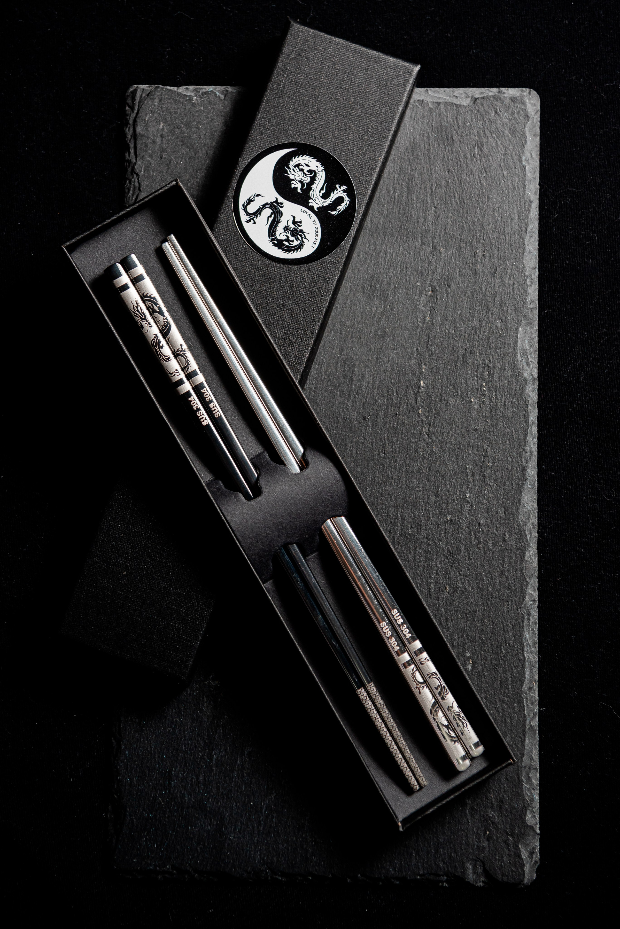 китайские палочки из нержавейки с гравировкой в виде дракона в картонной купаковке и на чёрном фоне
