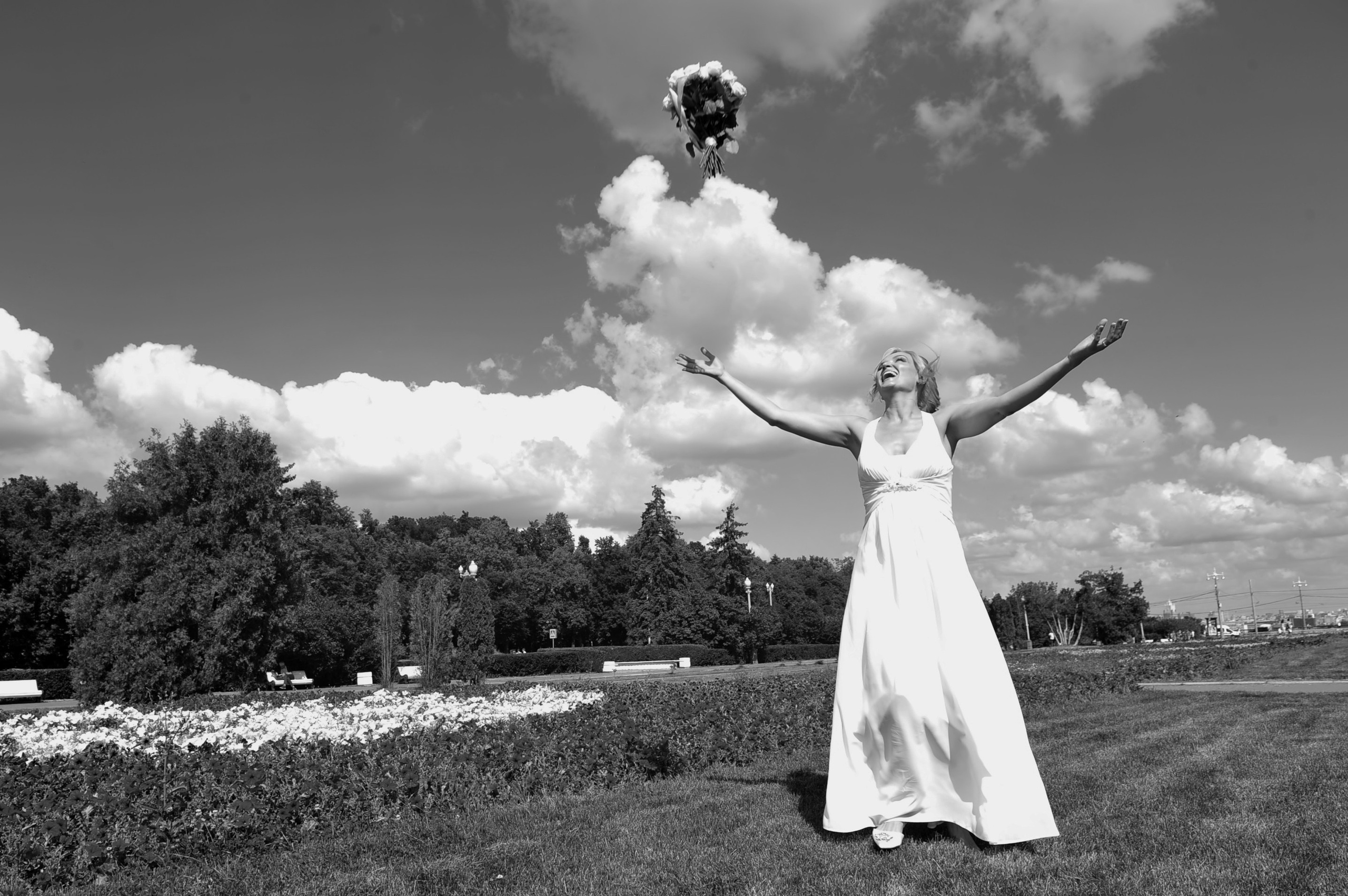 Свадьба на Воробьёвых Горах рядом с МГУ, невеста кидает свадебный букет на фоне облаков, черно-белая фотография