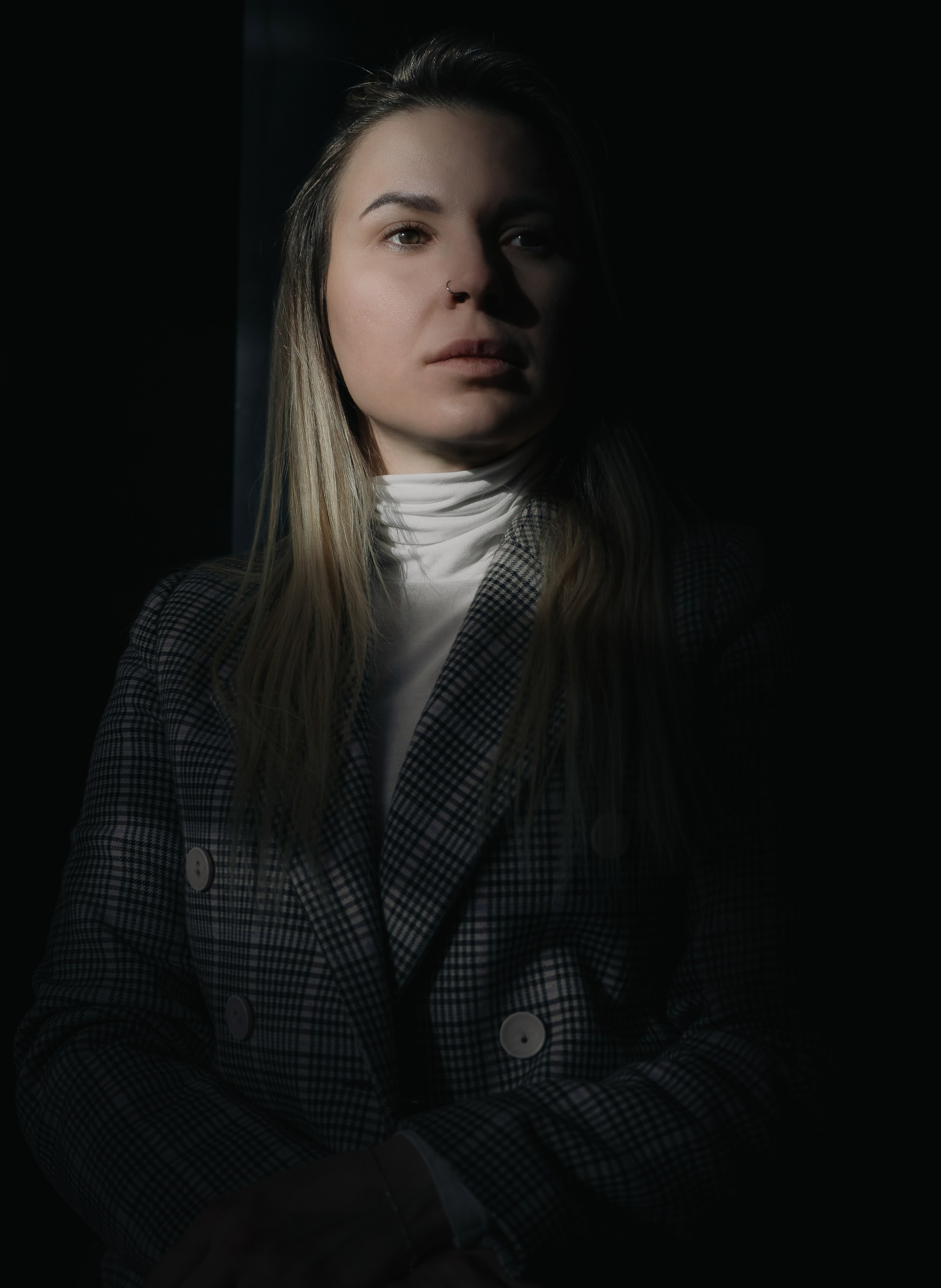 Драматичный портрет девушки с пирсингом в носу в тёмном помещении, свет падает сбоку, тёплый свитер и клетчатый пиджак, студийный портрет Санкт-Петербург. фотограф Мальцев Евгений. 