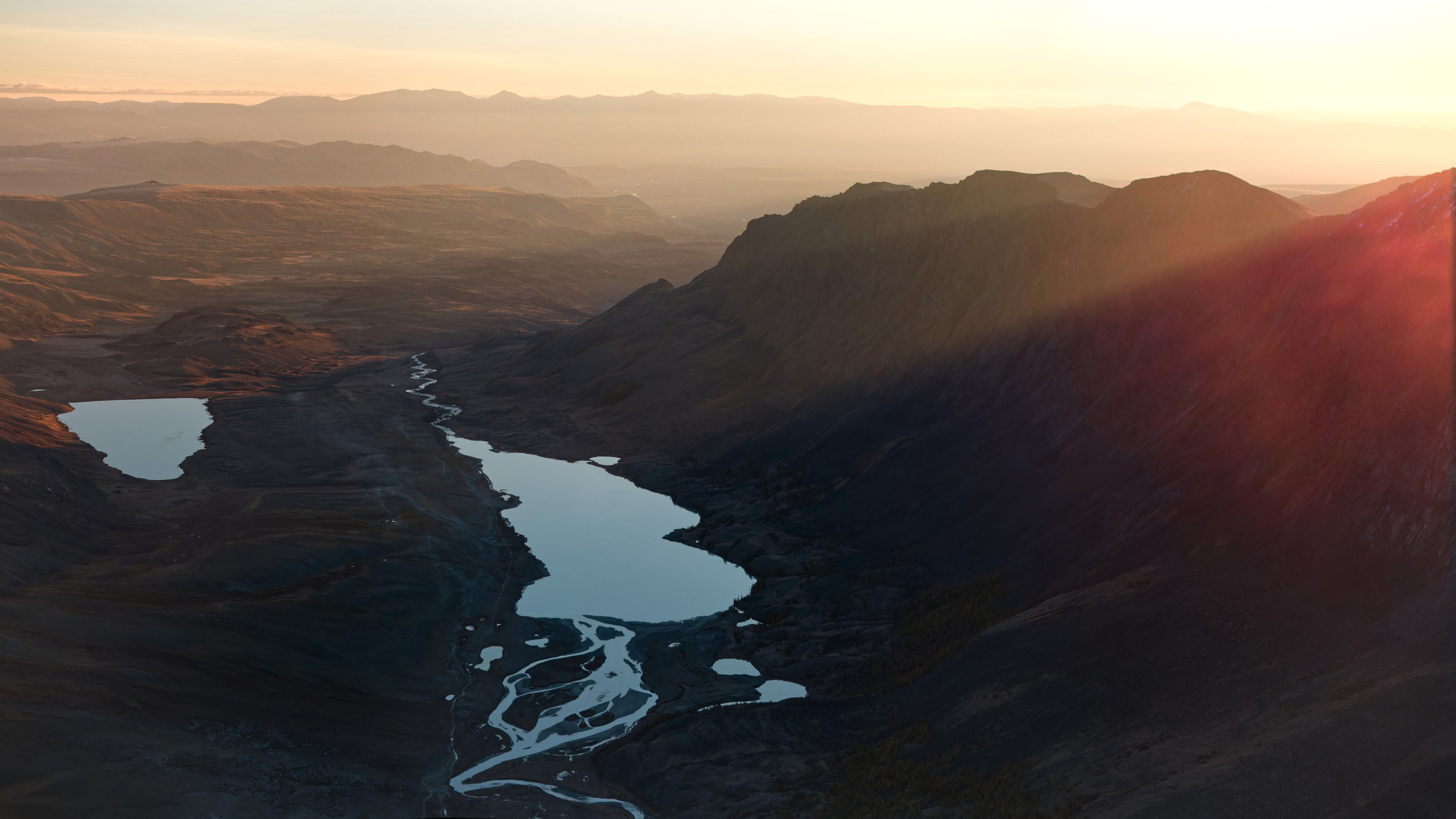 Рассвет в ущелье, на переднем плане озера в тени, луч солнца, выходящий из-за горы и освещающий холмы на заднем плане