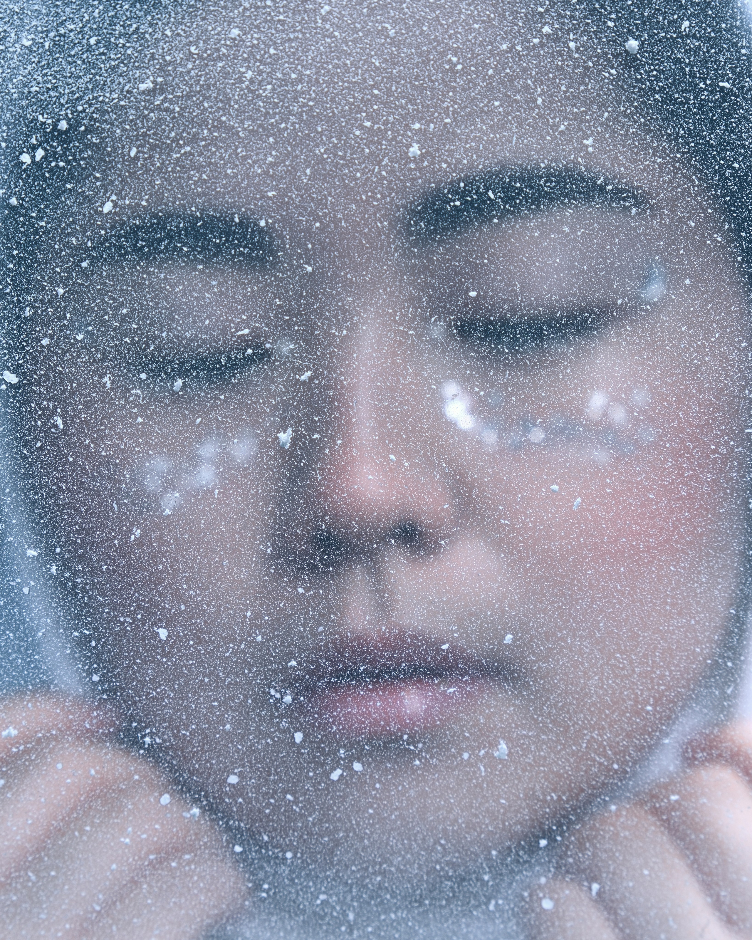 Крупный план героини фотосессии в стиле K-Pop: мягкий свет, зимний образ, на заднем плане — падающий снег и синий фон. Съёмка по мотивам White Midnight ENHYPEN в Санкт-Петербурге