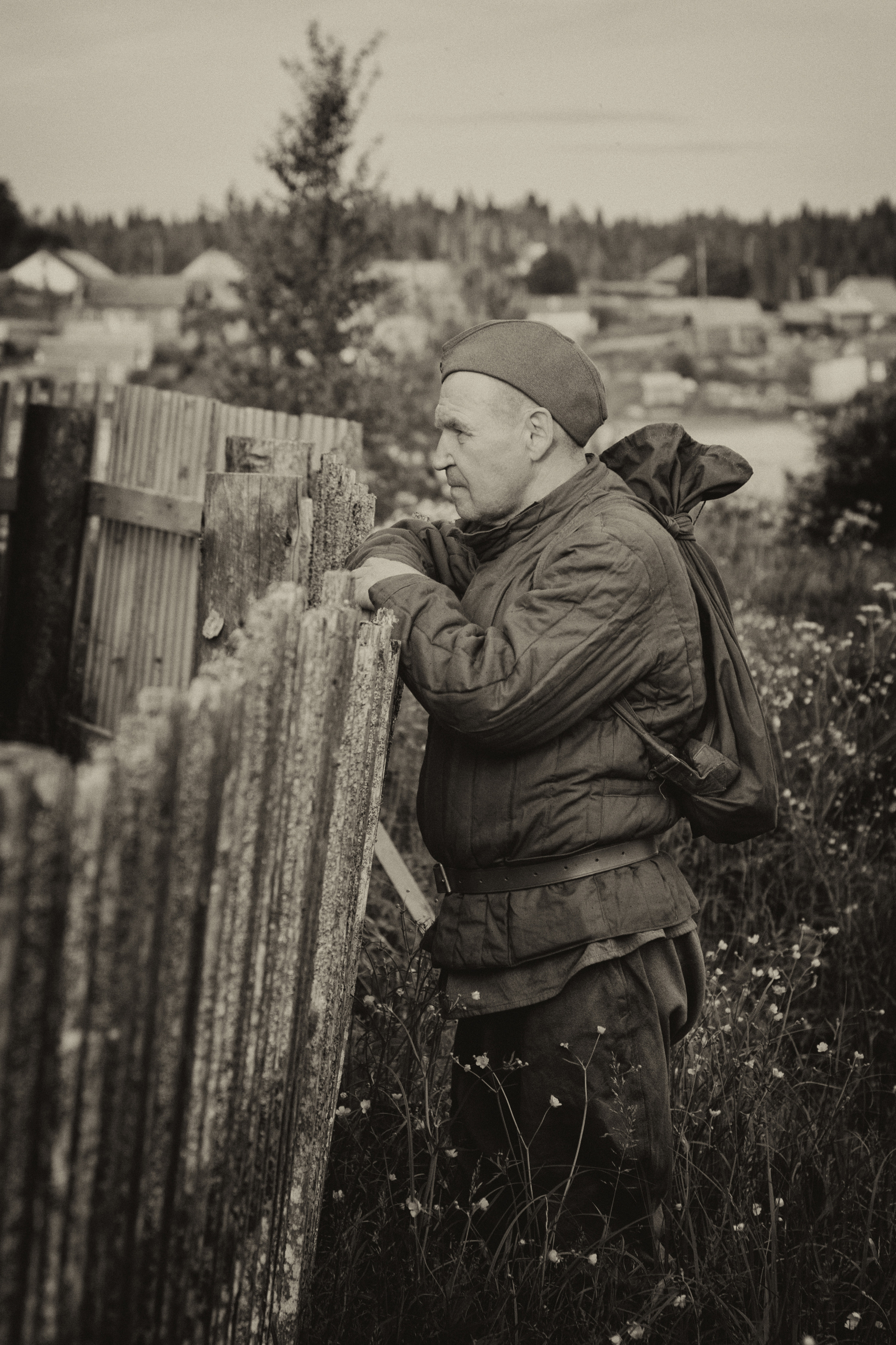 Солдат с вещмешком стоит у забора дома. Вернулся с войны.