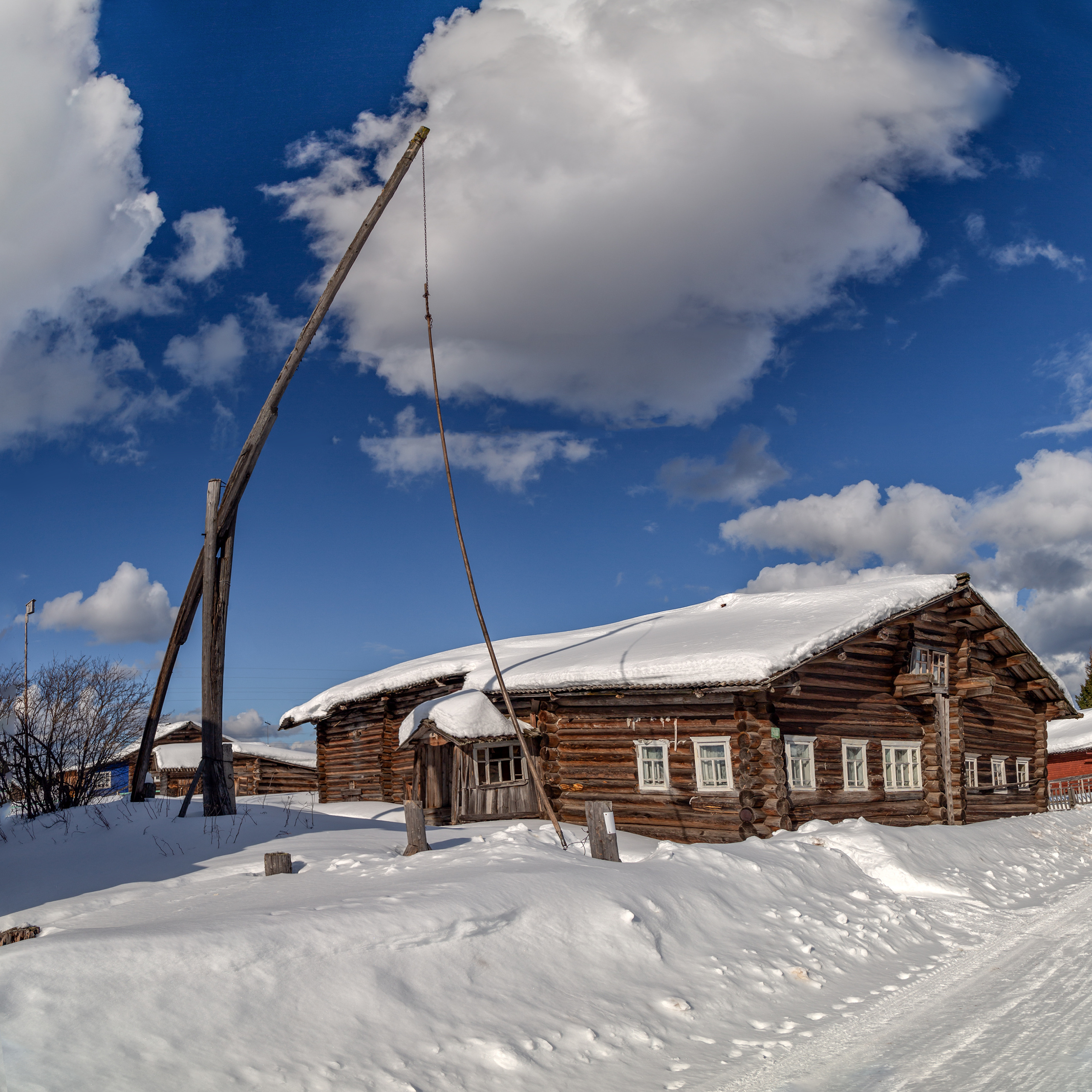 Колодец - журавель во дворе дома зимой.