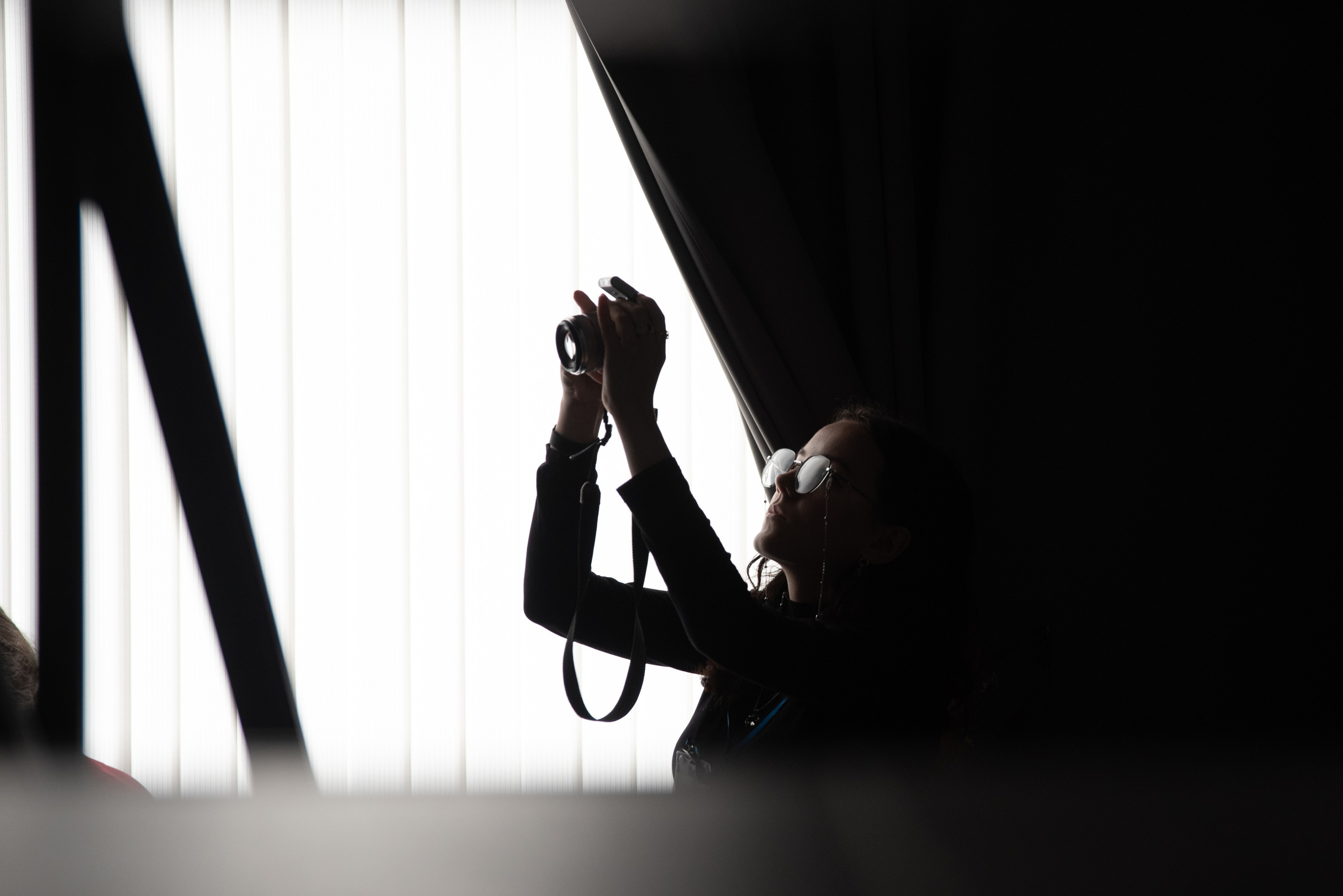 Девушка с фотоаппаратом напротив окна. Блики в стёклах очков.