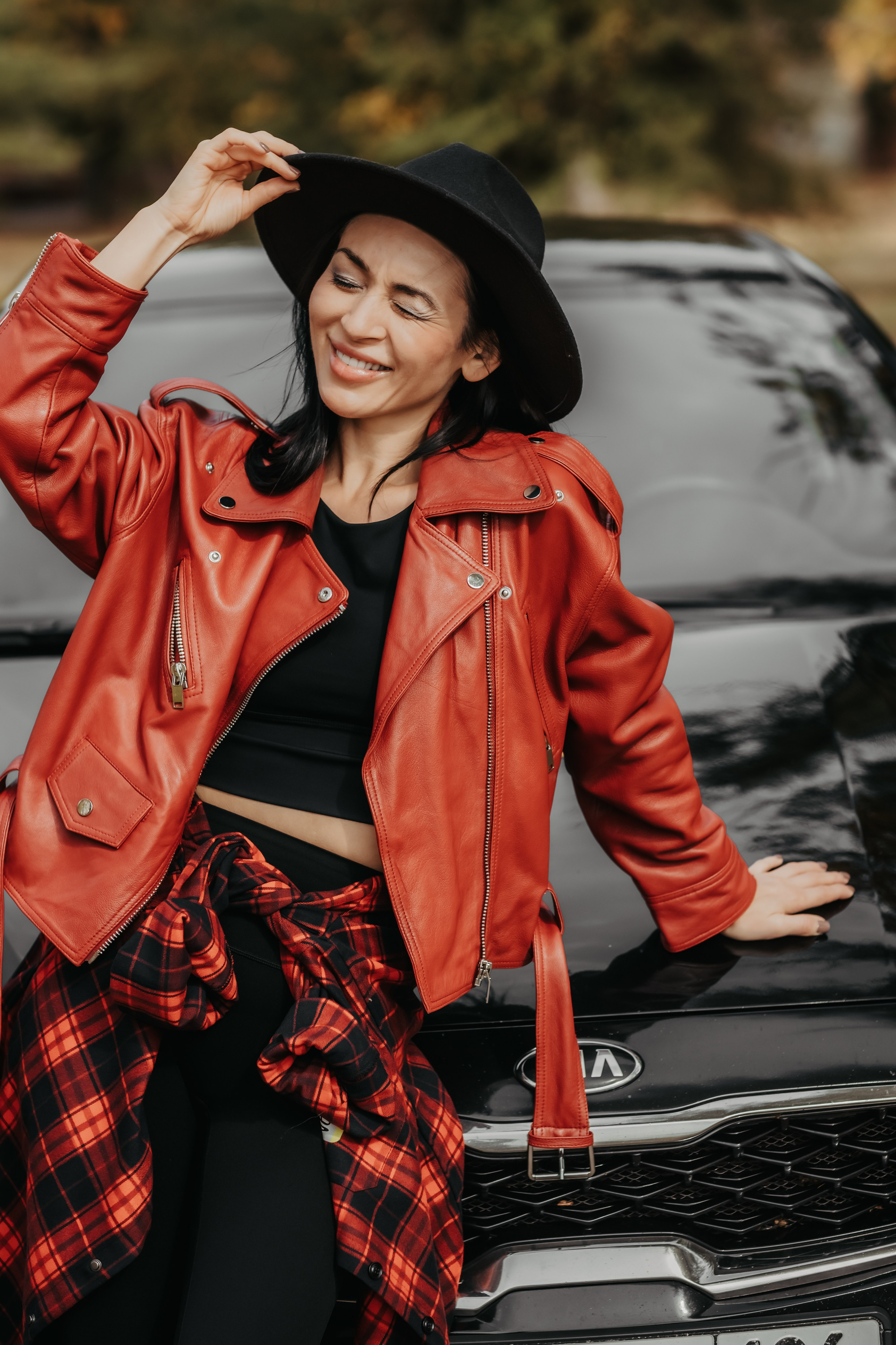 Молодая женщина в осеннем наряде позирует возле своего автомобиля на фоне яркой листвы Невинномысска