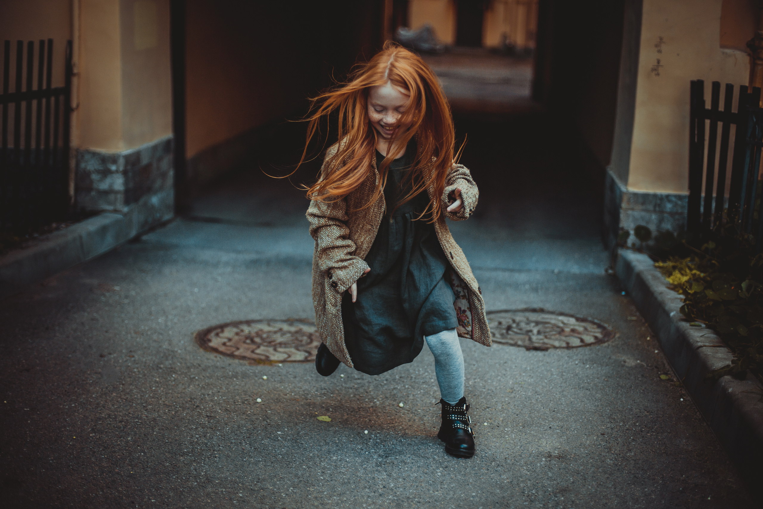 длинноволосая рыжая девочка в пальто бежит через двор