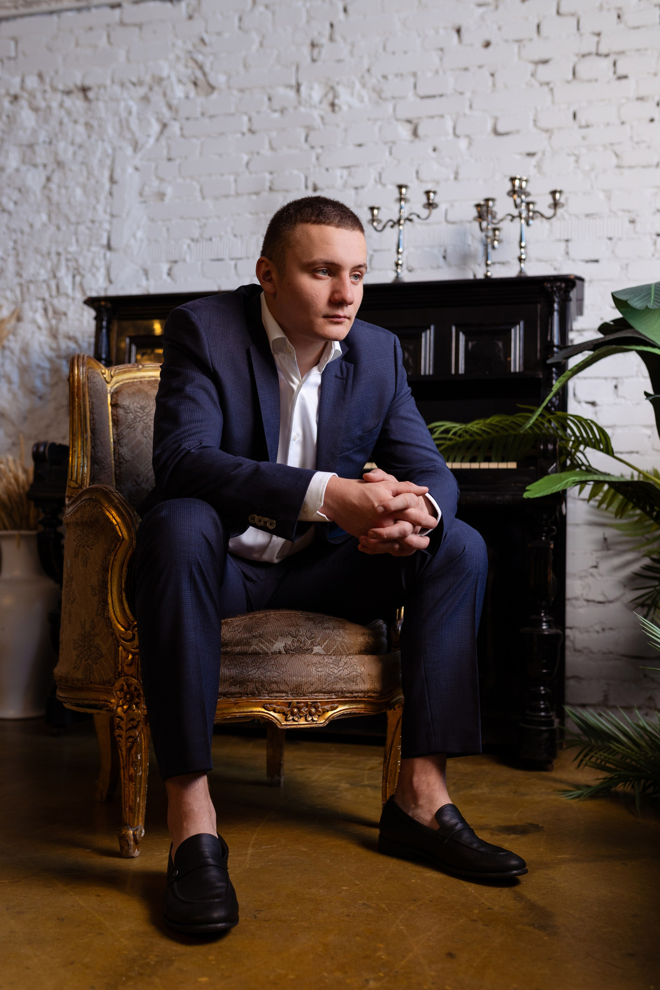 Жених сидит на стуле на фоне черного пианино.