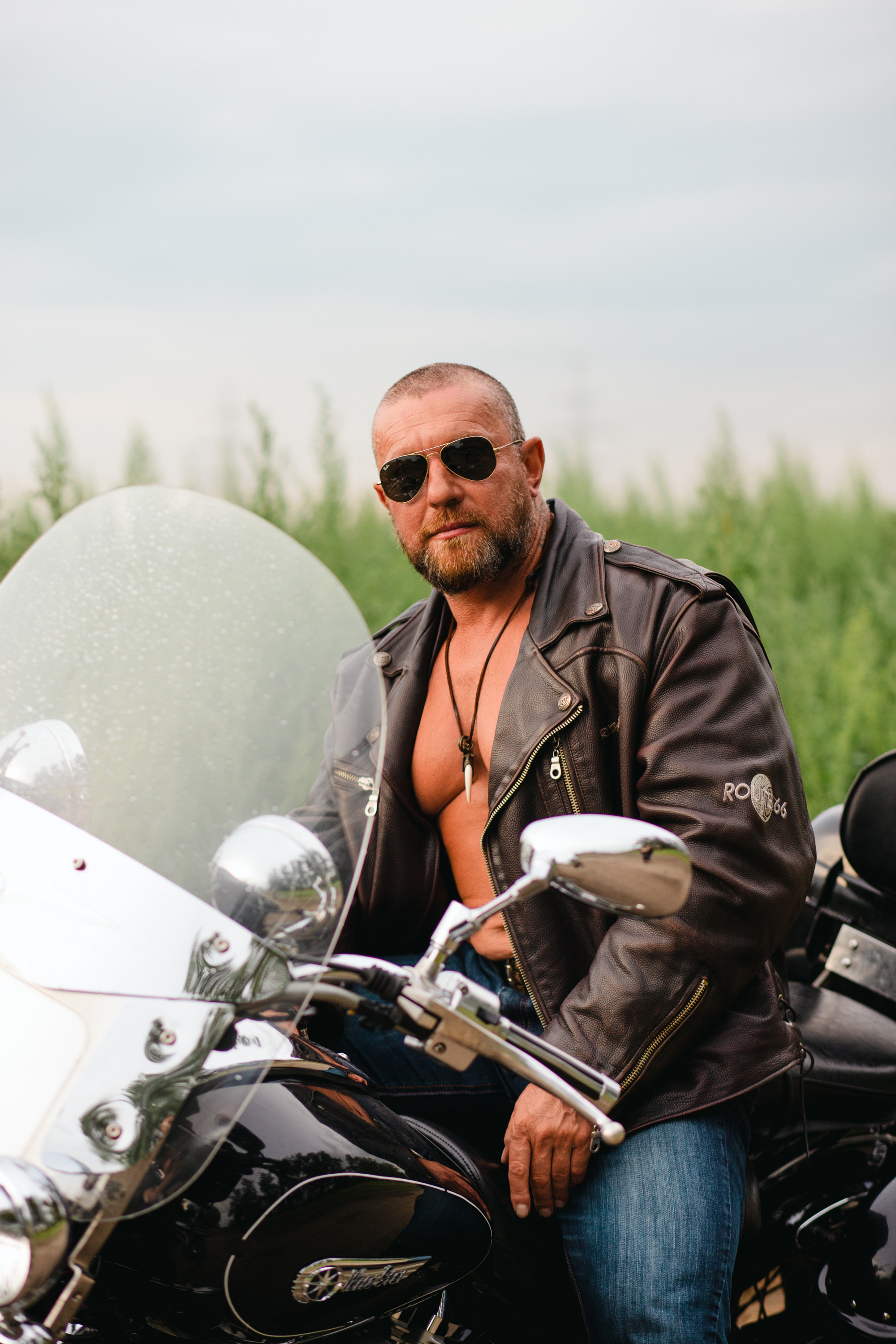 Мужчина в кожаной куртке на мотоцикле летом.