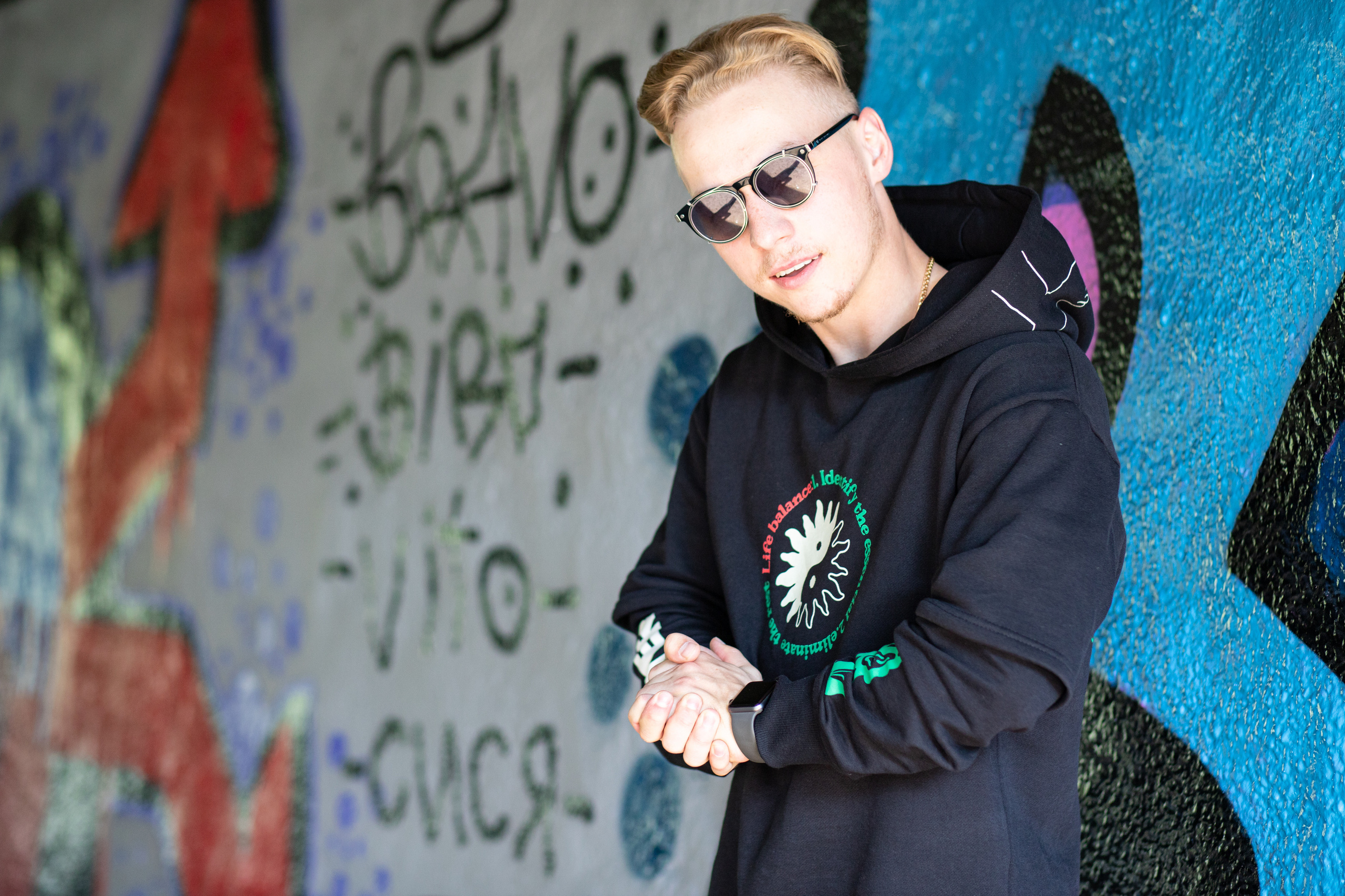 Парень в очках и синей толстовке на фоне стены с граффити. 