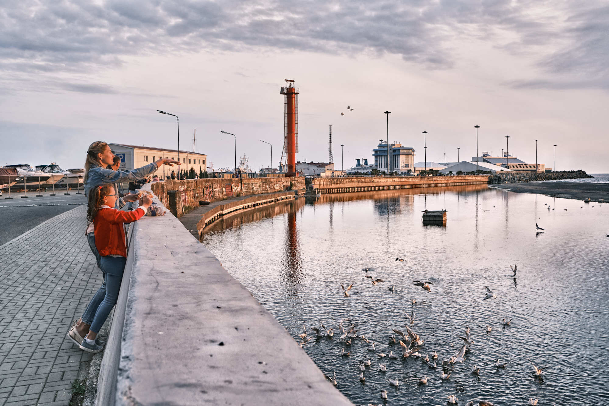 Sunset. The mouth of the Sochinka River. Passers-by feed the seagulls by throwing bread crumbs into the water. (Закатое время. Устье реки Сочинки. Прохожие кормят чаек, бросая в воду хлебные крошки.)