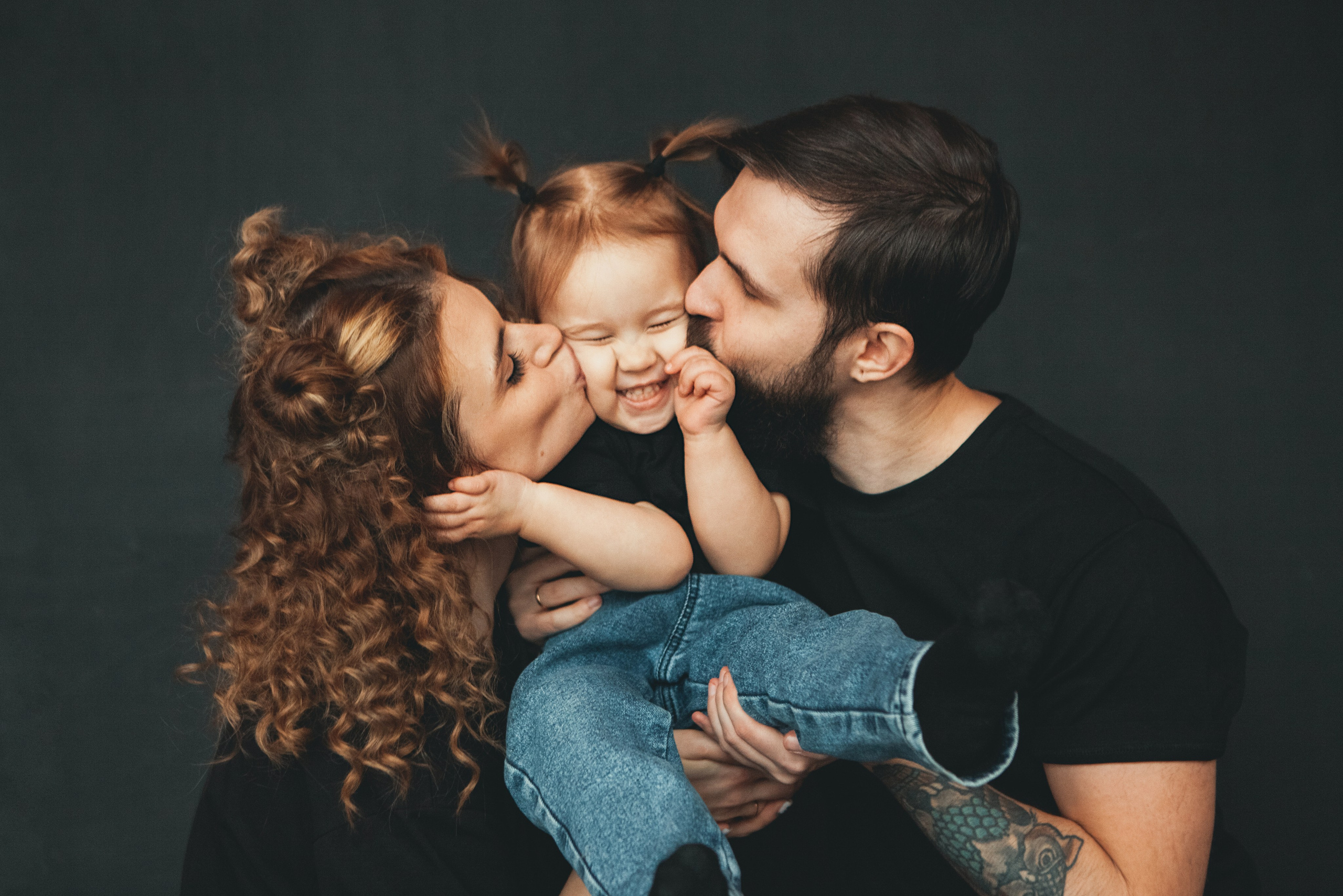 минимализм на семейной фотографии. Родители целуют дочку в обе щеки.