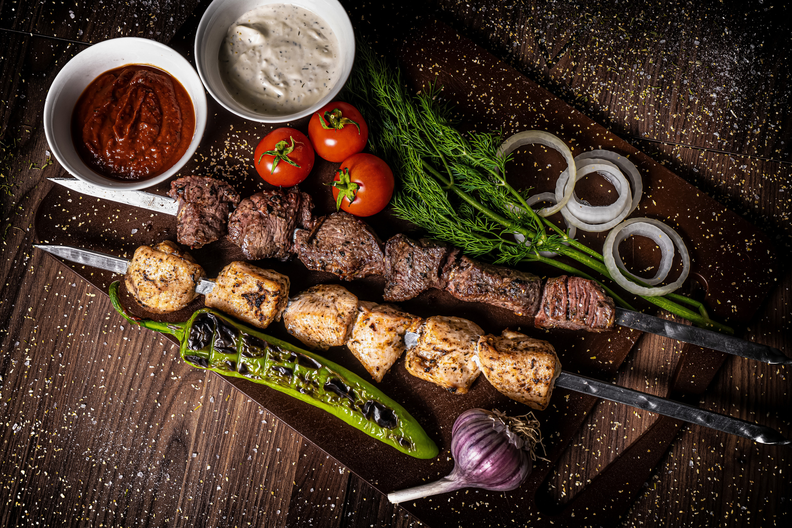 шашлык на доске в сервировке с помидорками черри, луком, чесноком, укропом, аджикой и мацони