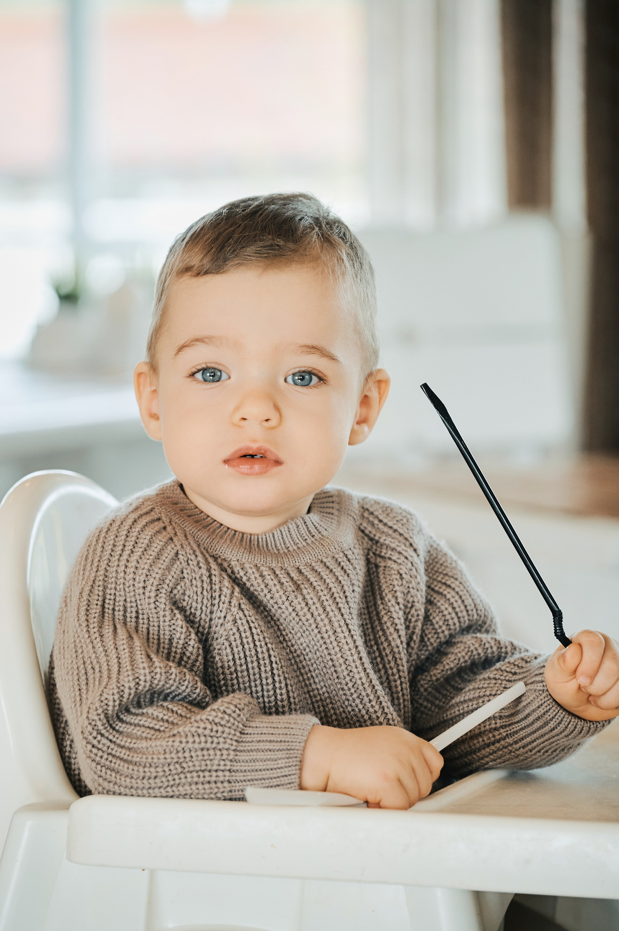 Портрет мальчика в вязаном свитере, он смотрит в камеру, держит трубочку и ложку.