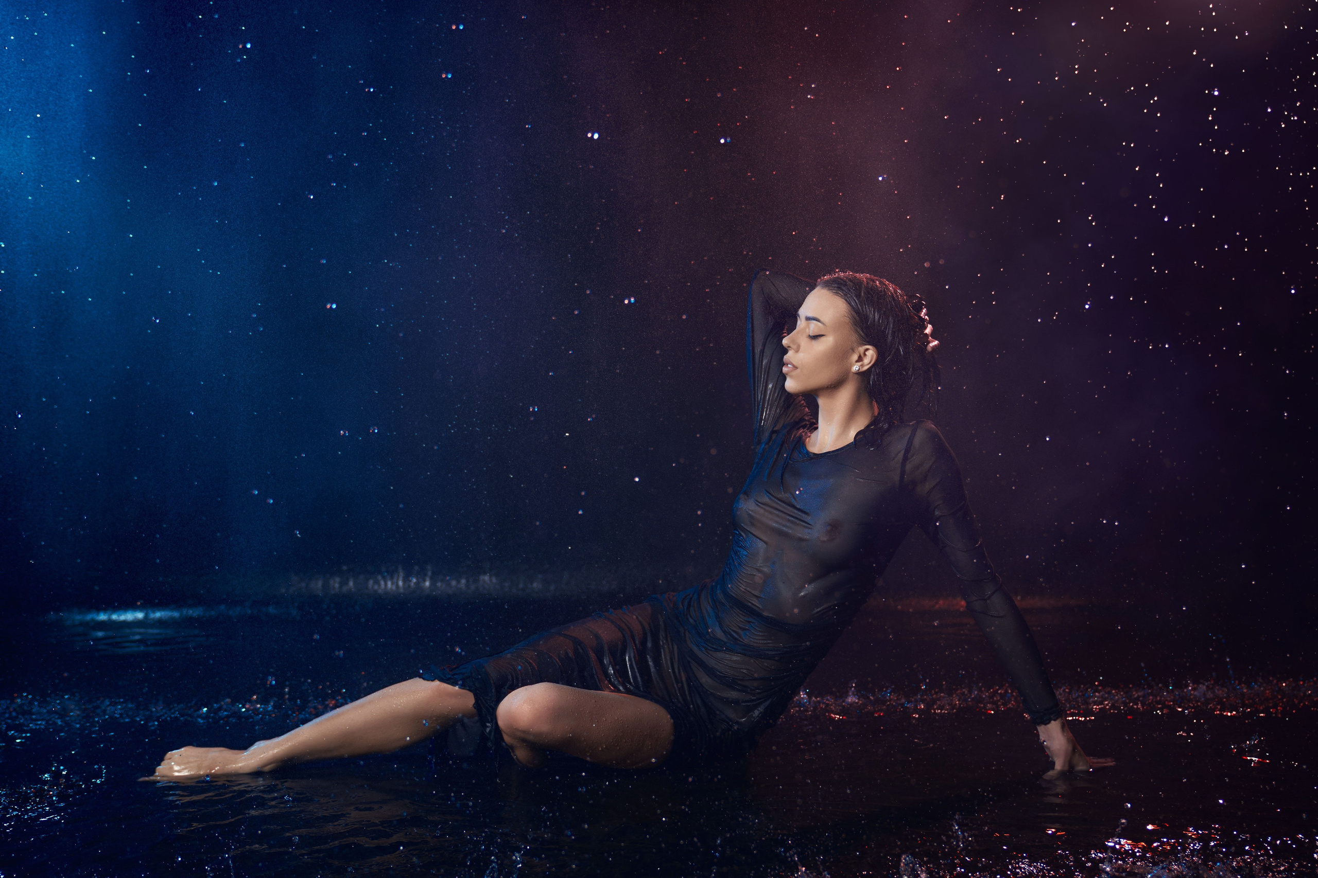 девушка в мокром полупрозрачном чёрном платье сидит в воде во время мокрой фотосессии