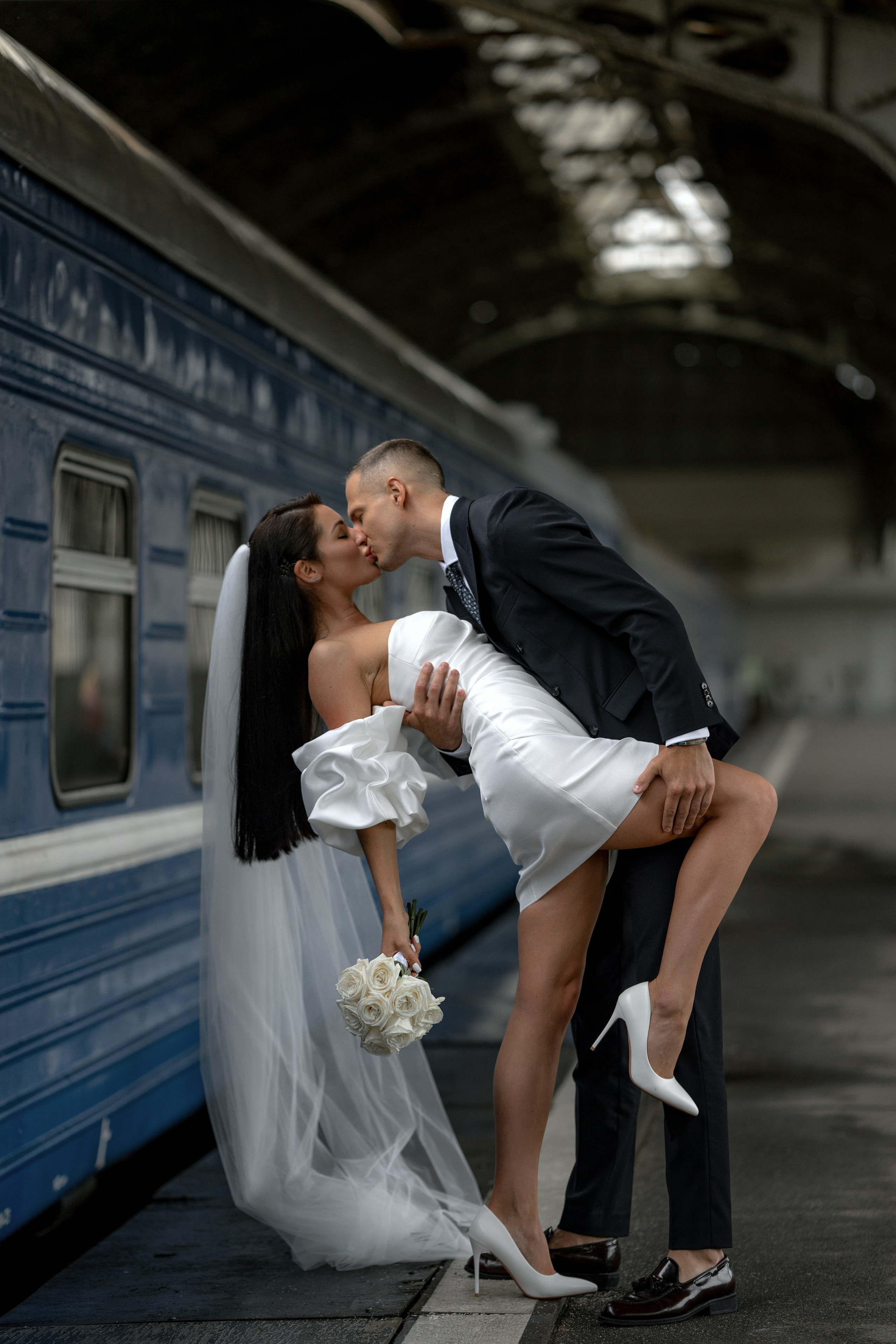 жених и невеста красиво целуются на перроне у синего поезда