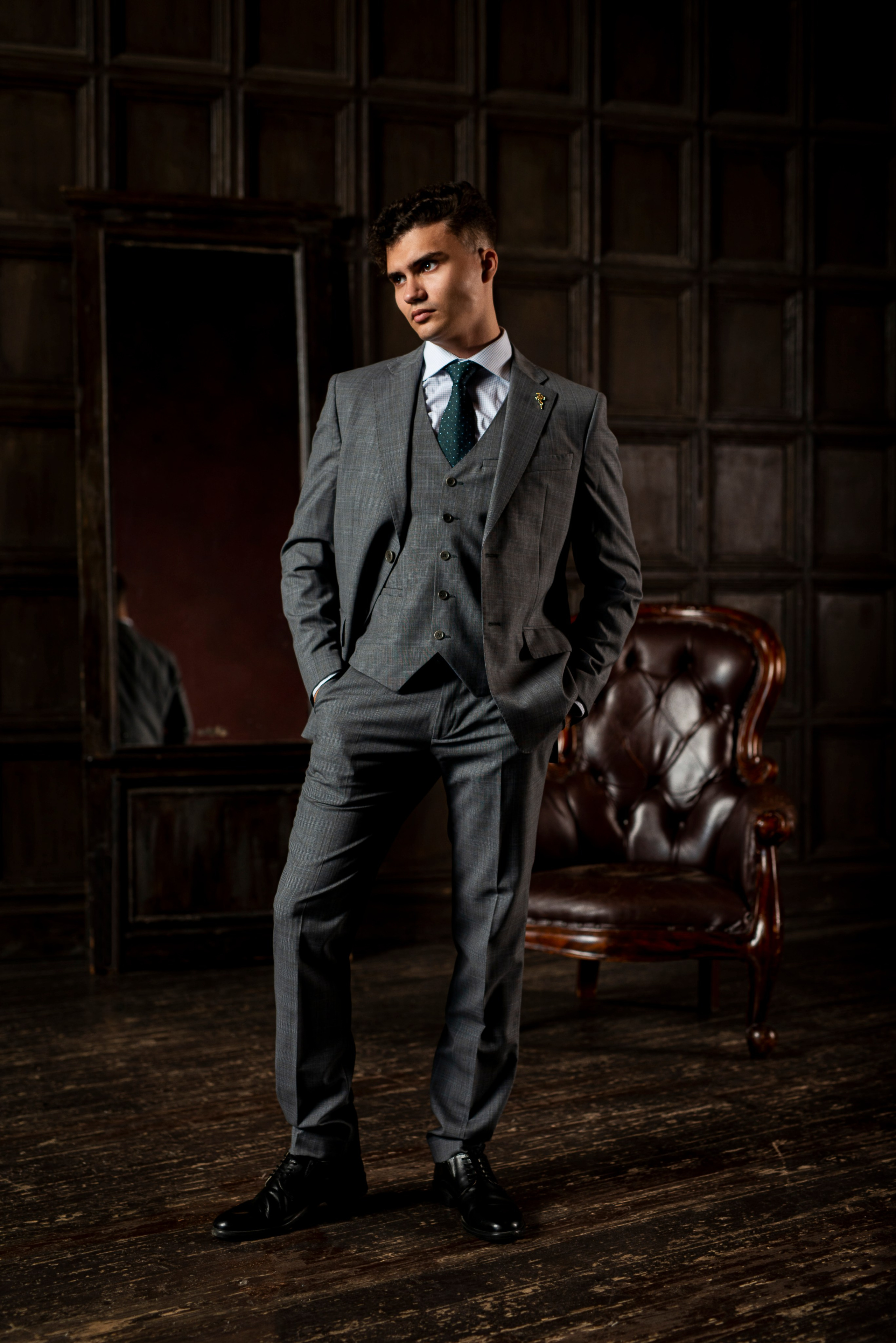 Молодой человек стоит в полный рост позируя в фотостудии во время съёмки в костюме