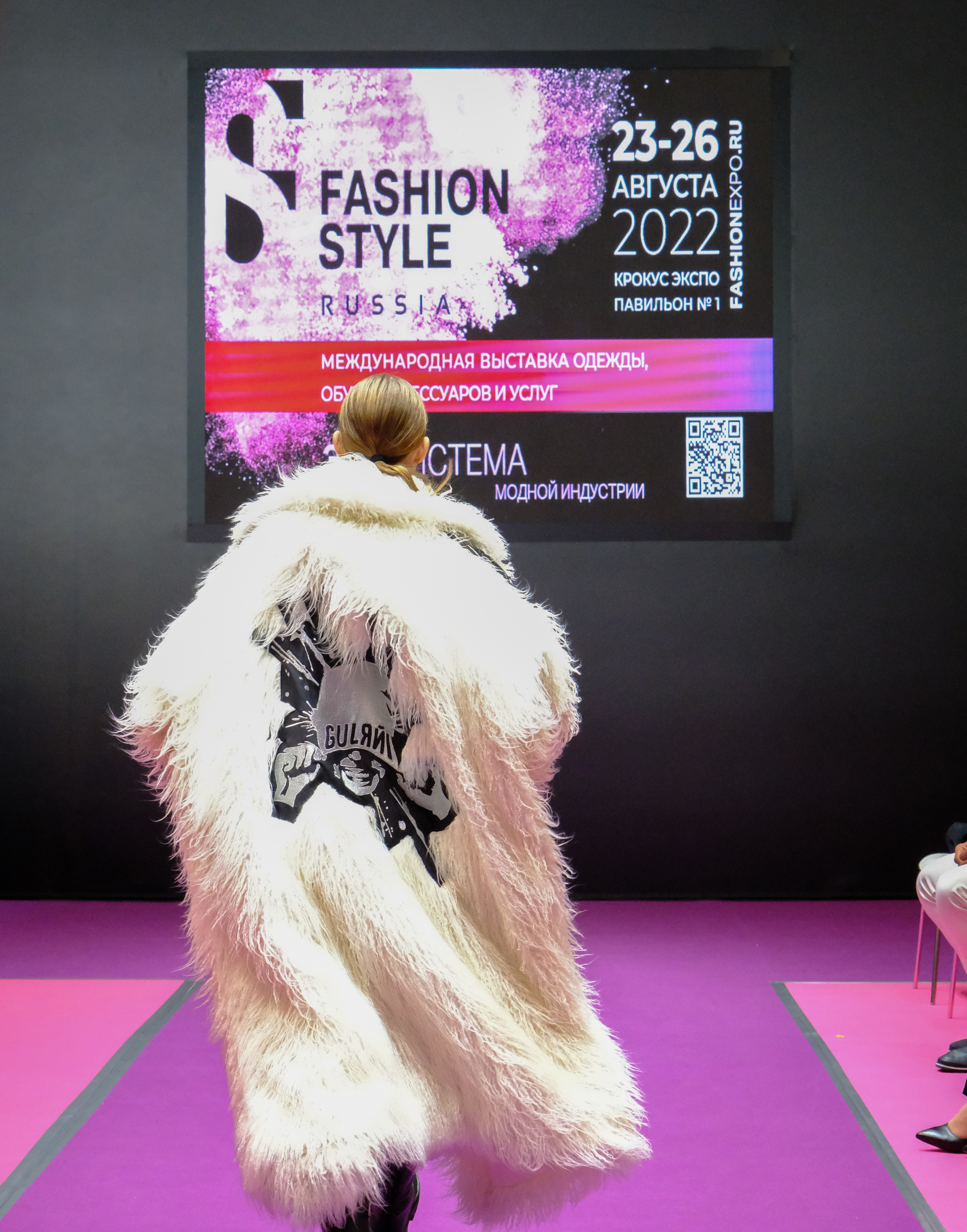  "Модели в ярких нарядах проходят по подиуму во время показа мод, освещенные яркими софитами и окруженные восторженными зрителями."