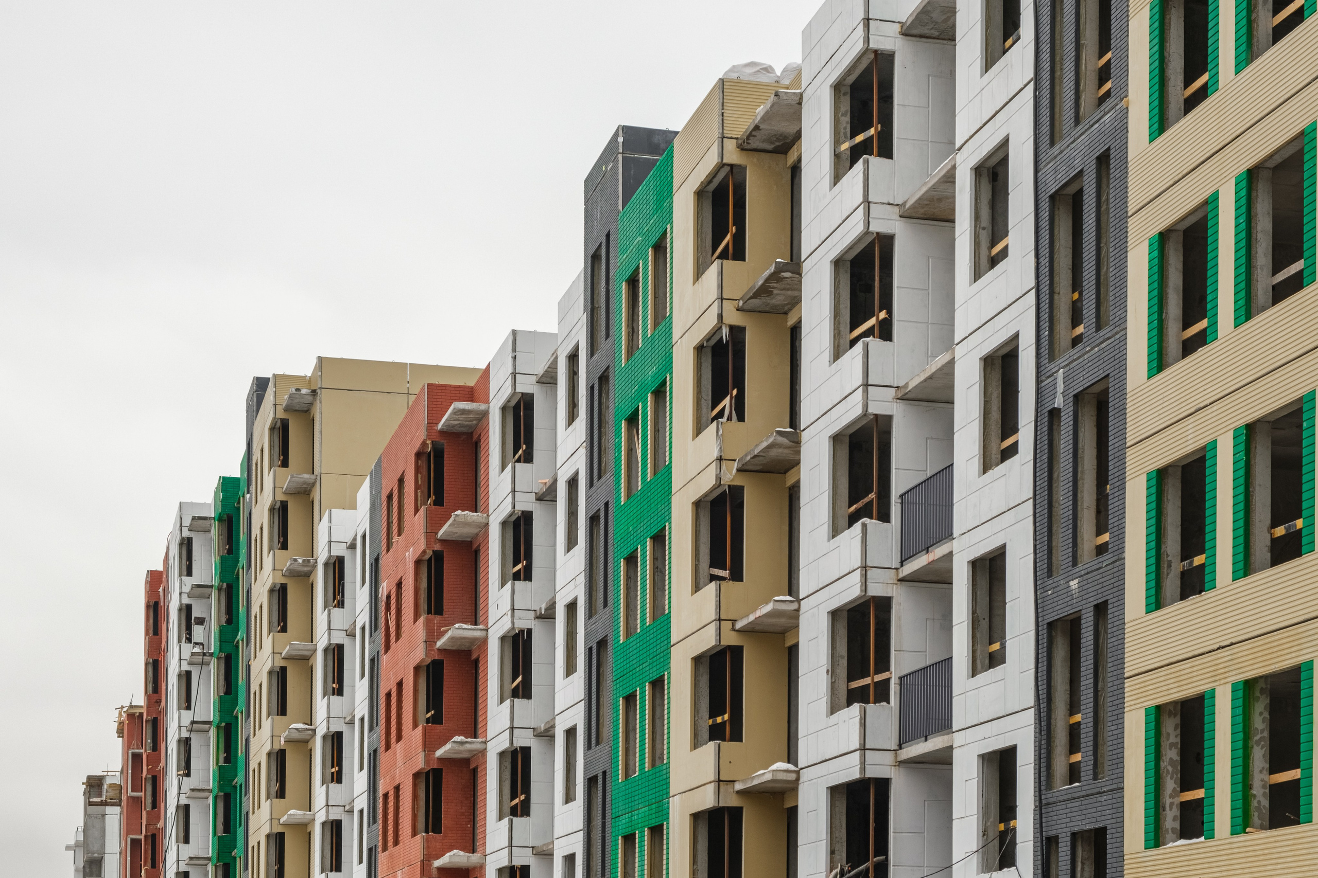 На изображении представлены многоквартирные жилые дома, выполненные в современном стиле. Каждый дом имеет уникальную цветовую гамму фасада.