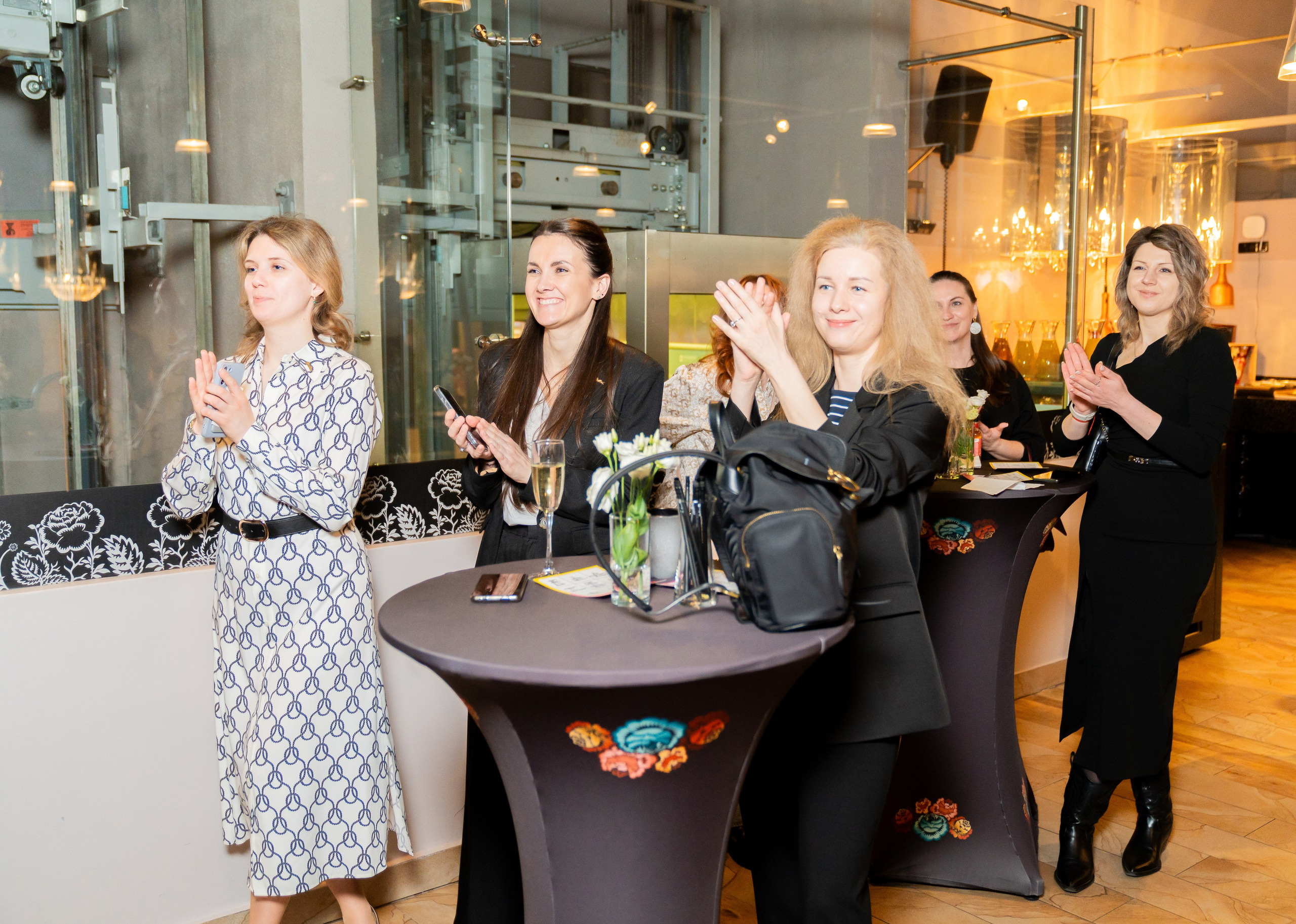 Женщины аплодируют стоя у высокого стола на корпоративном мероприятии в Radisson Sonya. Фотограф Евгений Мальцев.