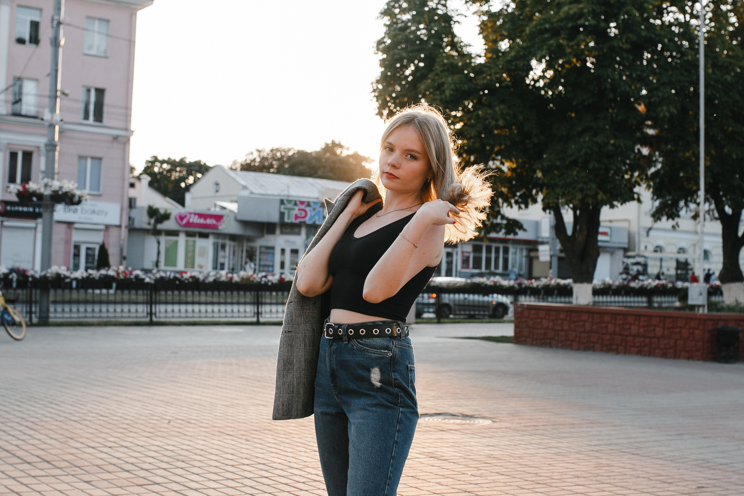 стройная девушка на закате в черной майке и джинсах шевелит волосами. Солнечный день в городе, слегка пожелтевшие деревья