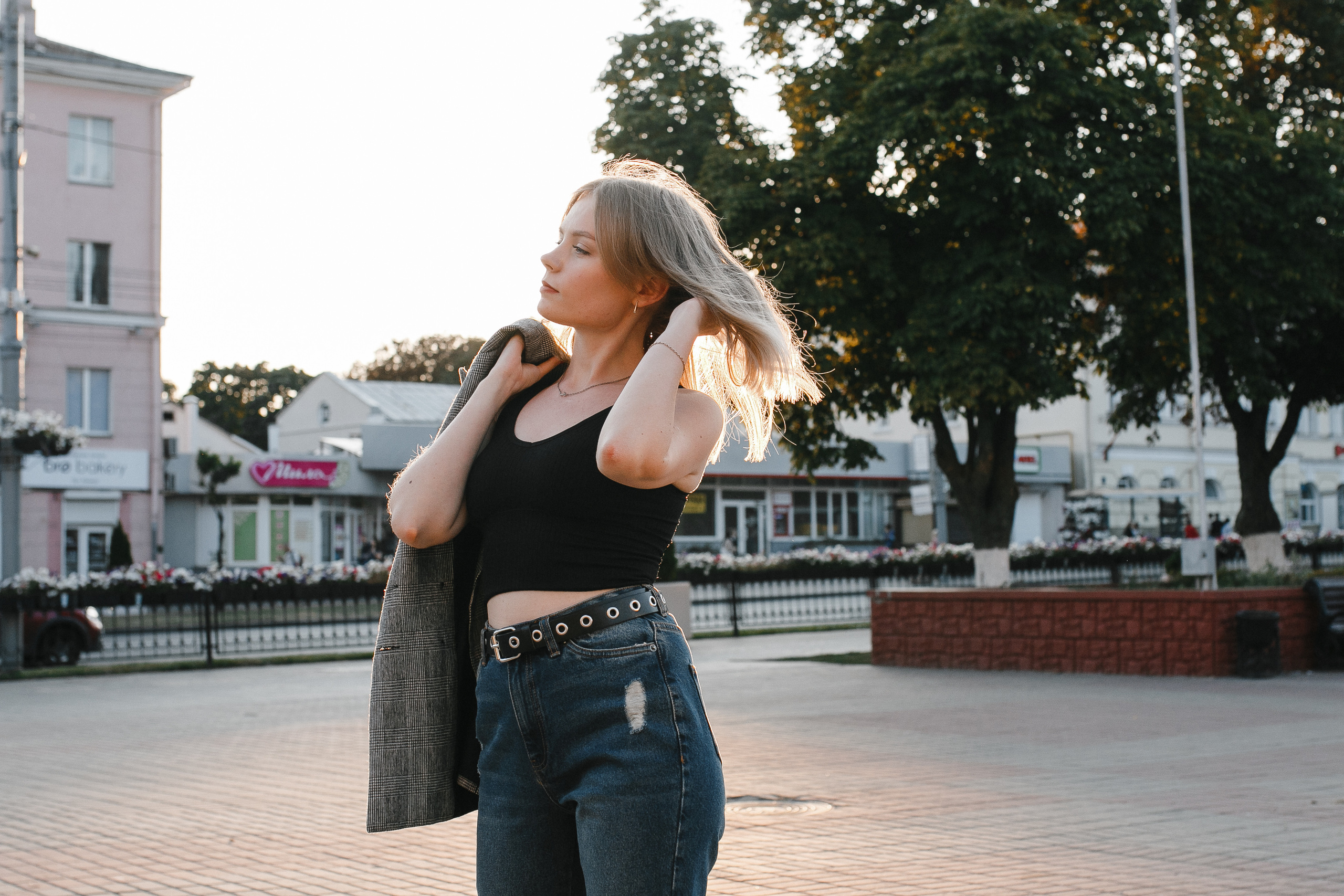 стройная девушка на закате в черной майке и джинсах шевелит волосами. Солнечный день в городе, слегка пожелтевшие деревья