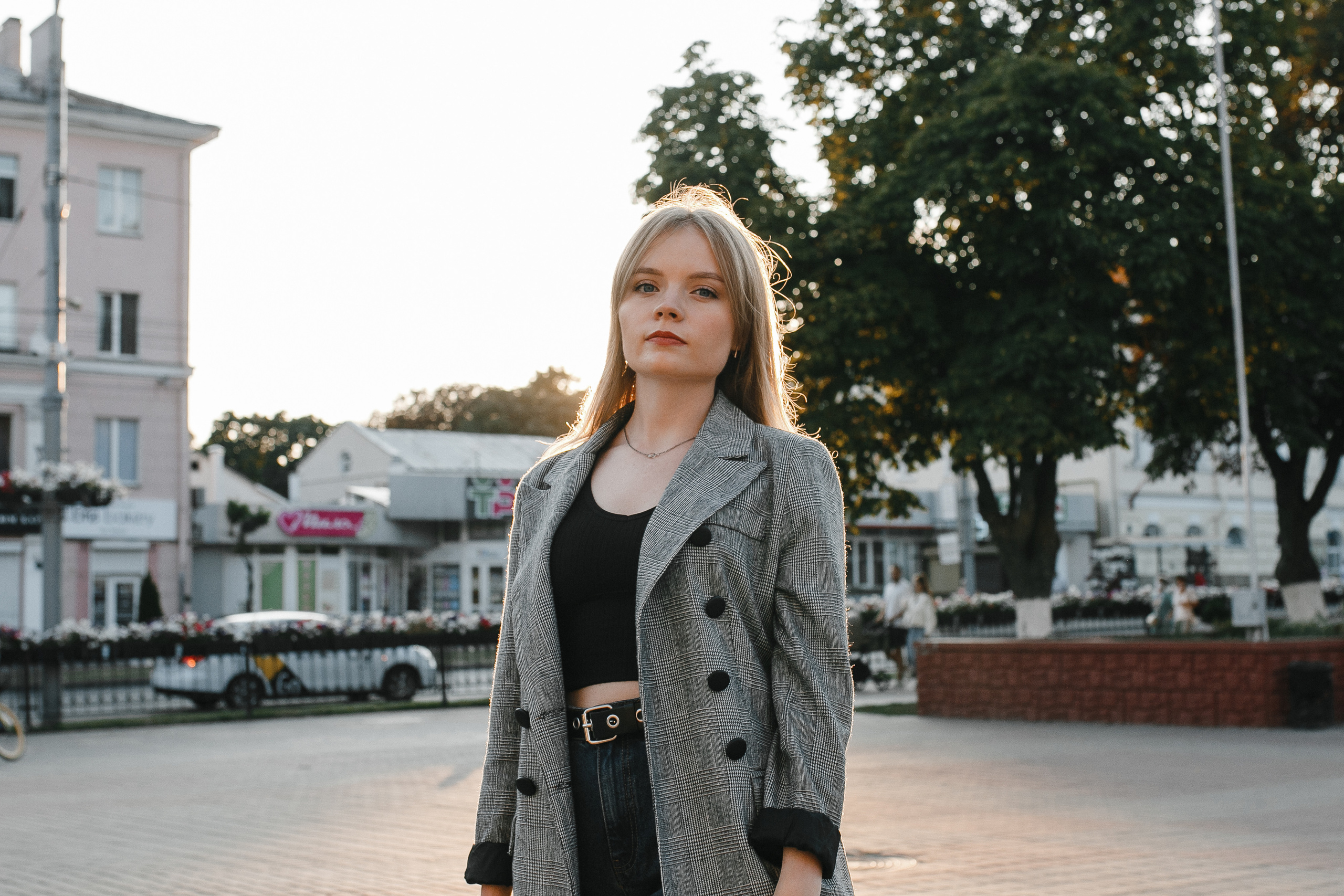 стройная девушка в сером пальто  и джинсах в лучах закатного солнца,пробивающегося сквозь городские здания и слегка пожелтевшие деревья