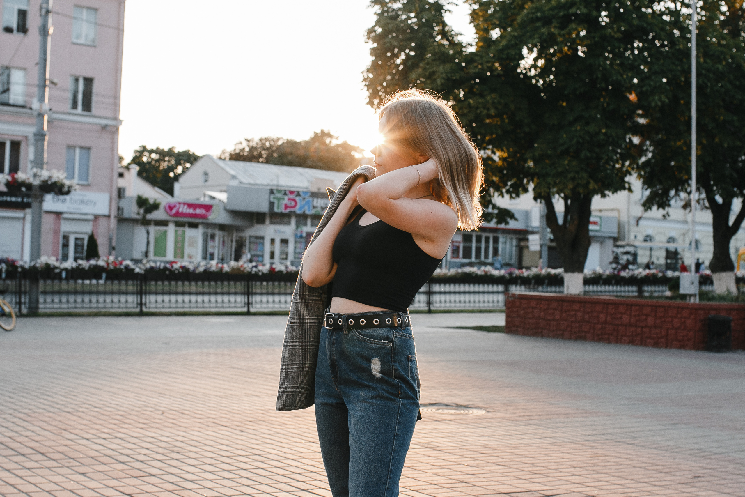 стройная девушка на закате в черной майке и джинсах шевелит волосами. Солнечный день в городе, слегка пожелтевшие деревья